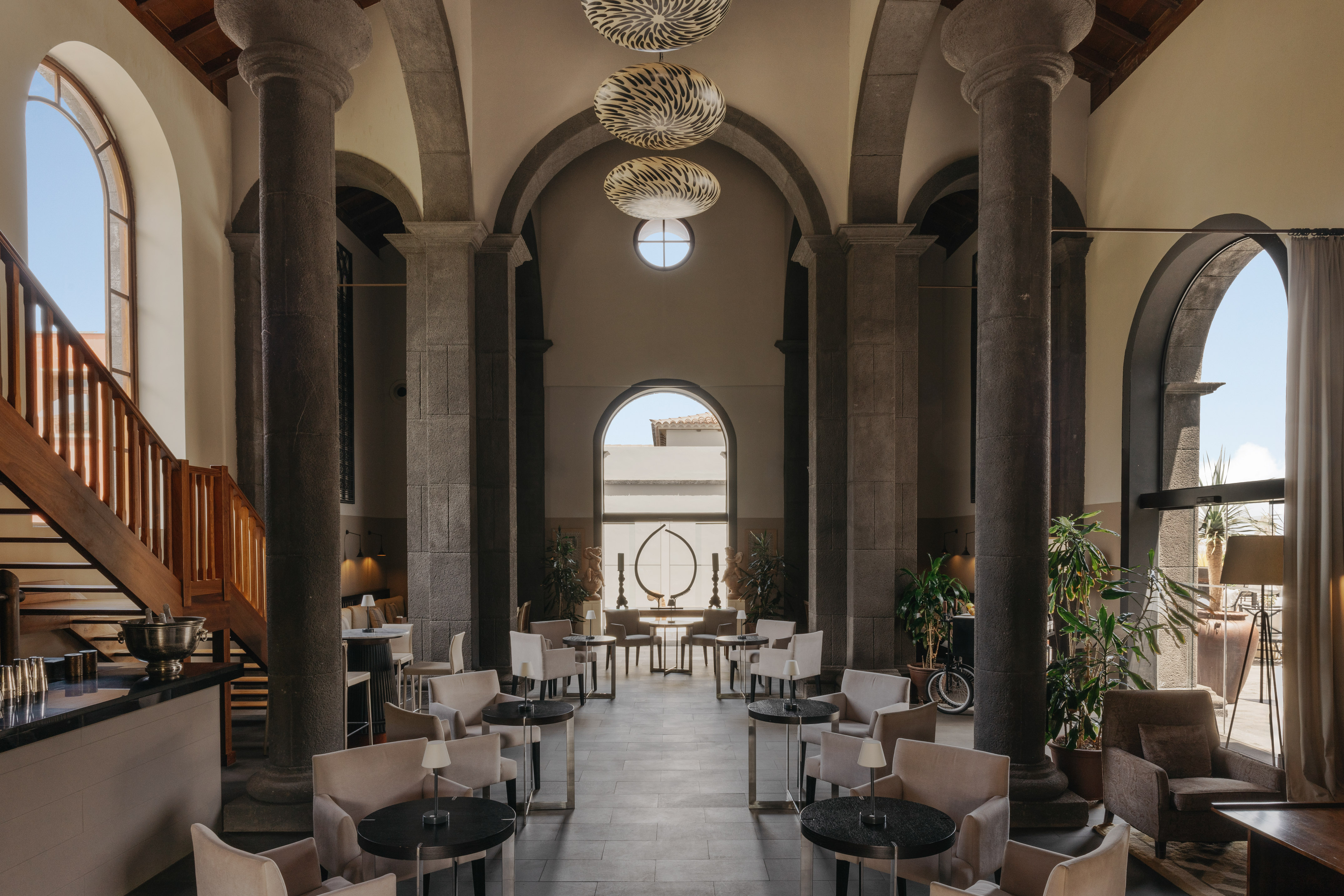 Elegant lounge with stone columns, arched windows, stylish seating, bar.