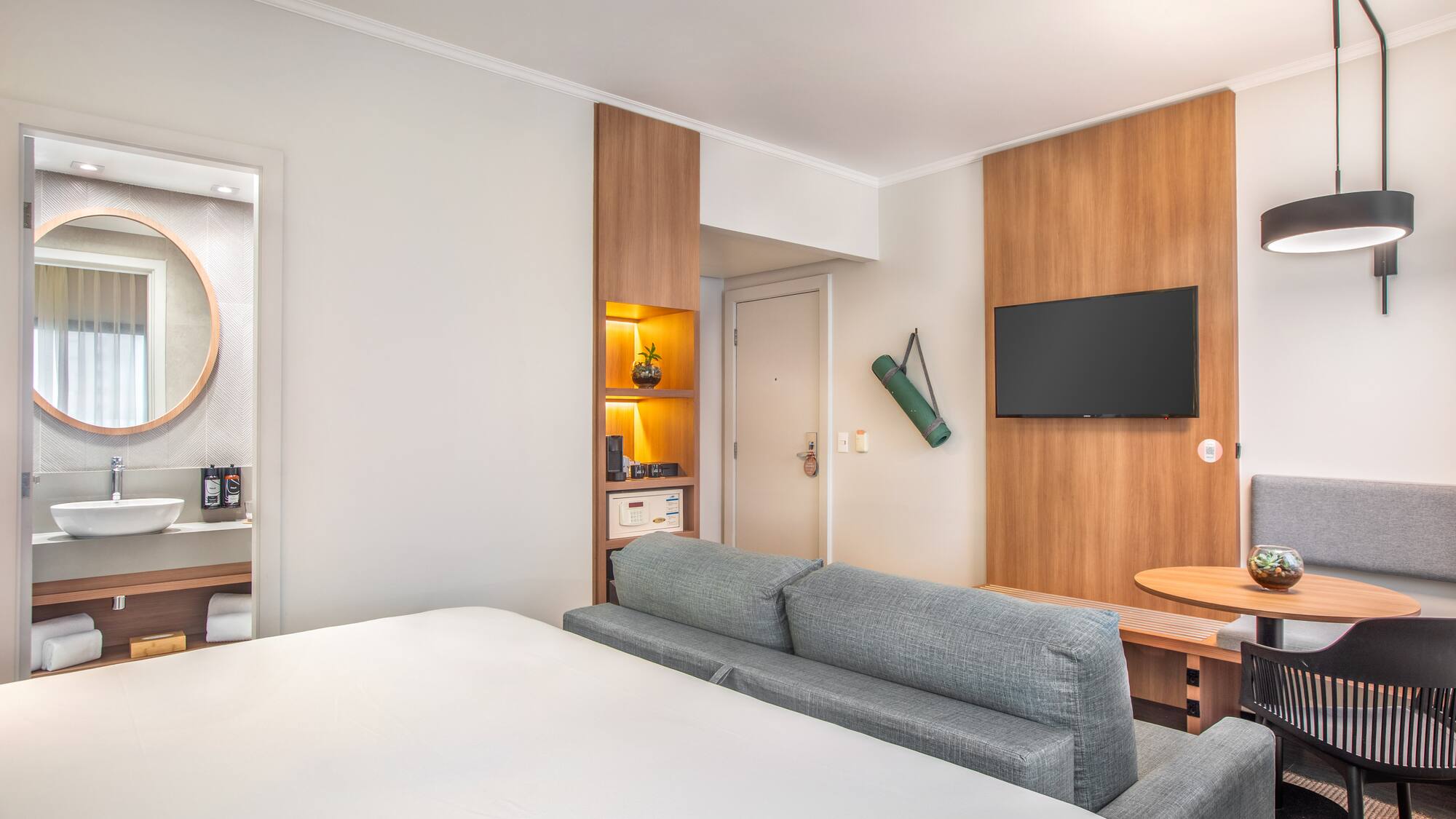 Modern hotel room with bed, sofa, smart TV, workspace, and integrated bathroom.