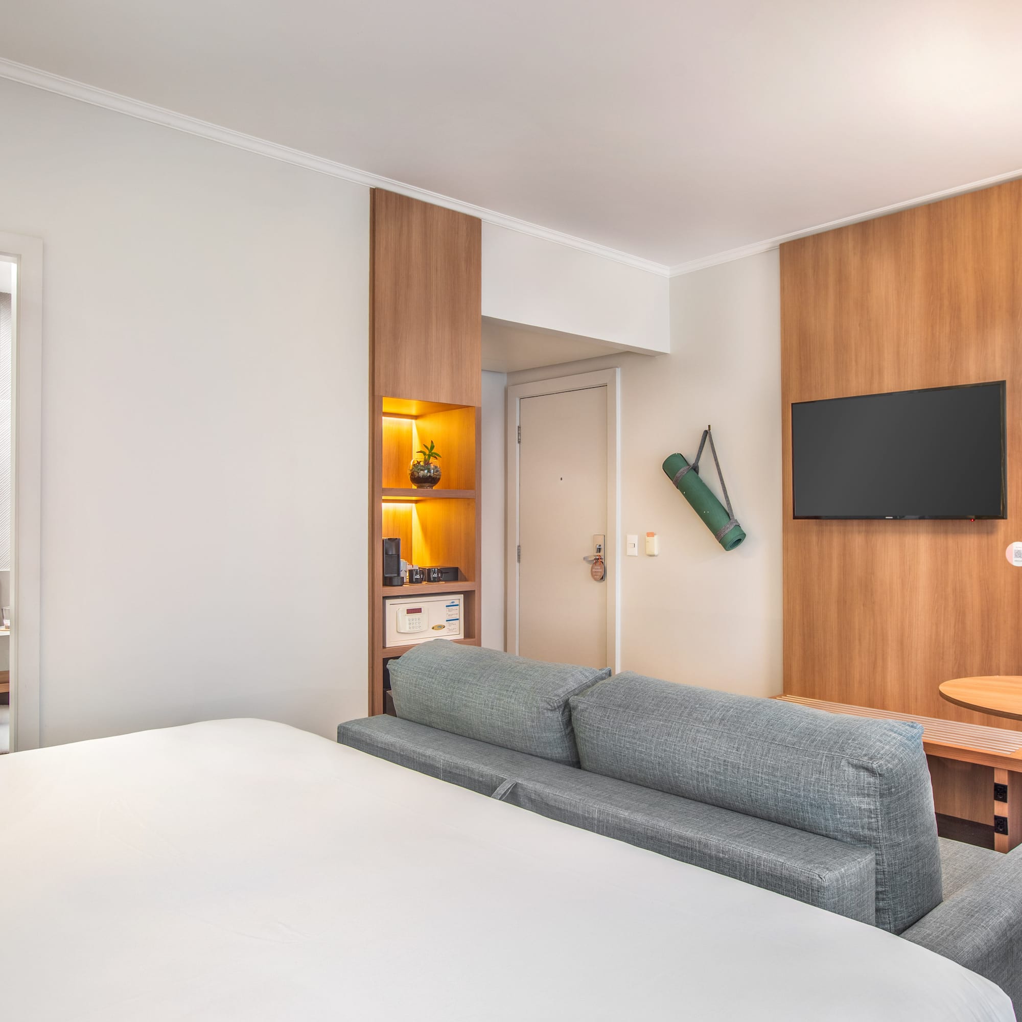 Habitación de hotel moderna con cama, sofá cama, TV, mesa y baño.