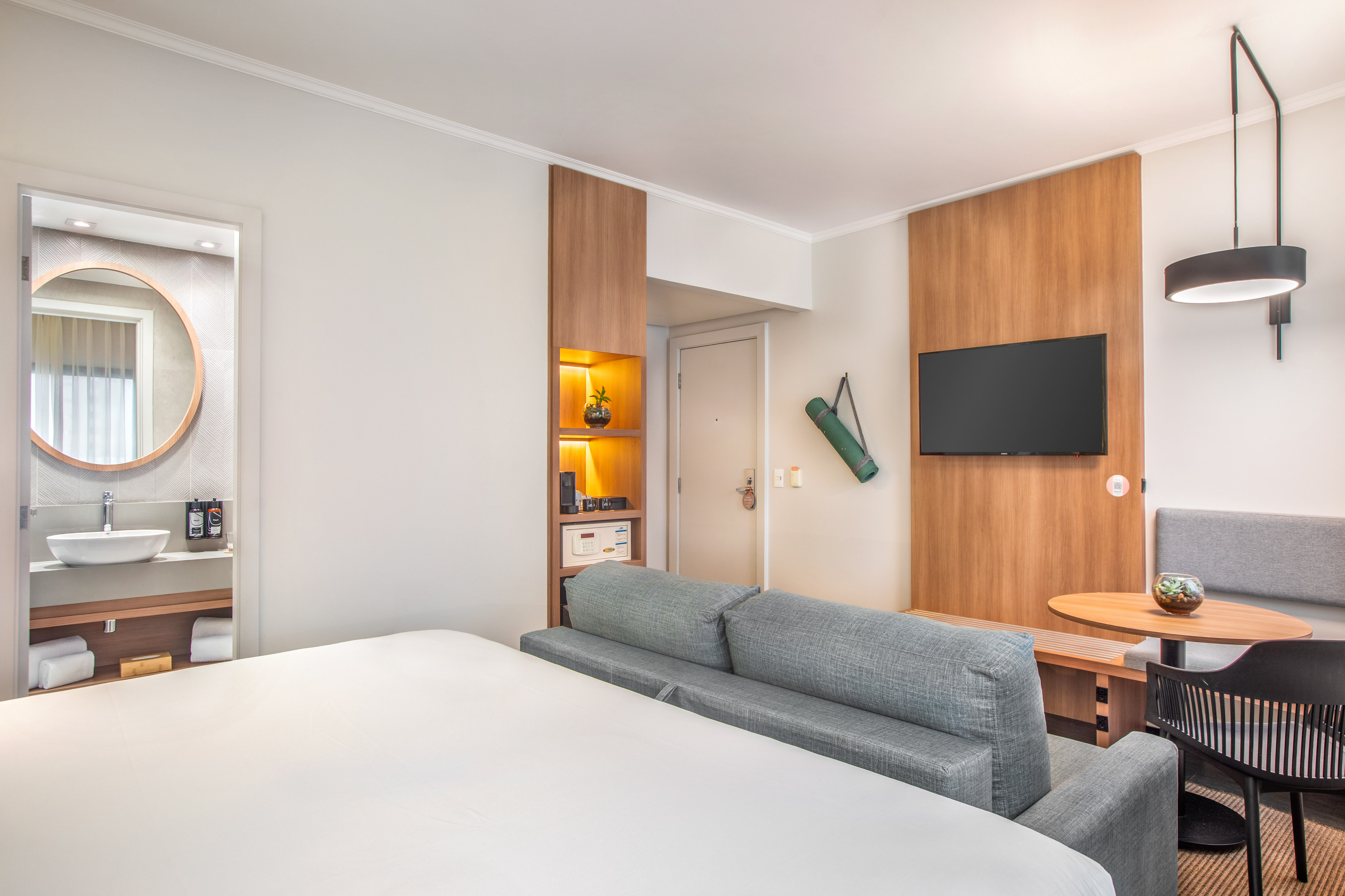 Habitación de hotel moderna con cama, sofá cama, TV, mesa y baño.