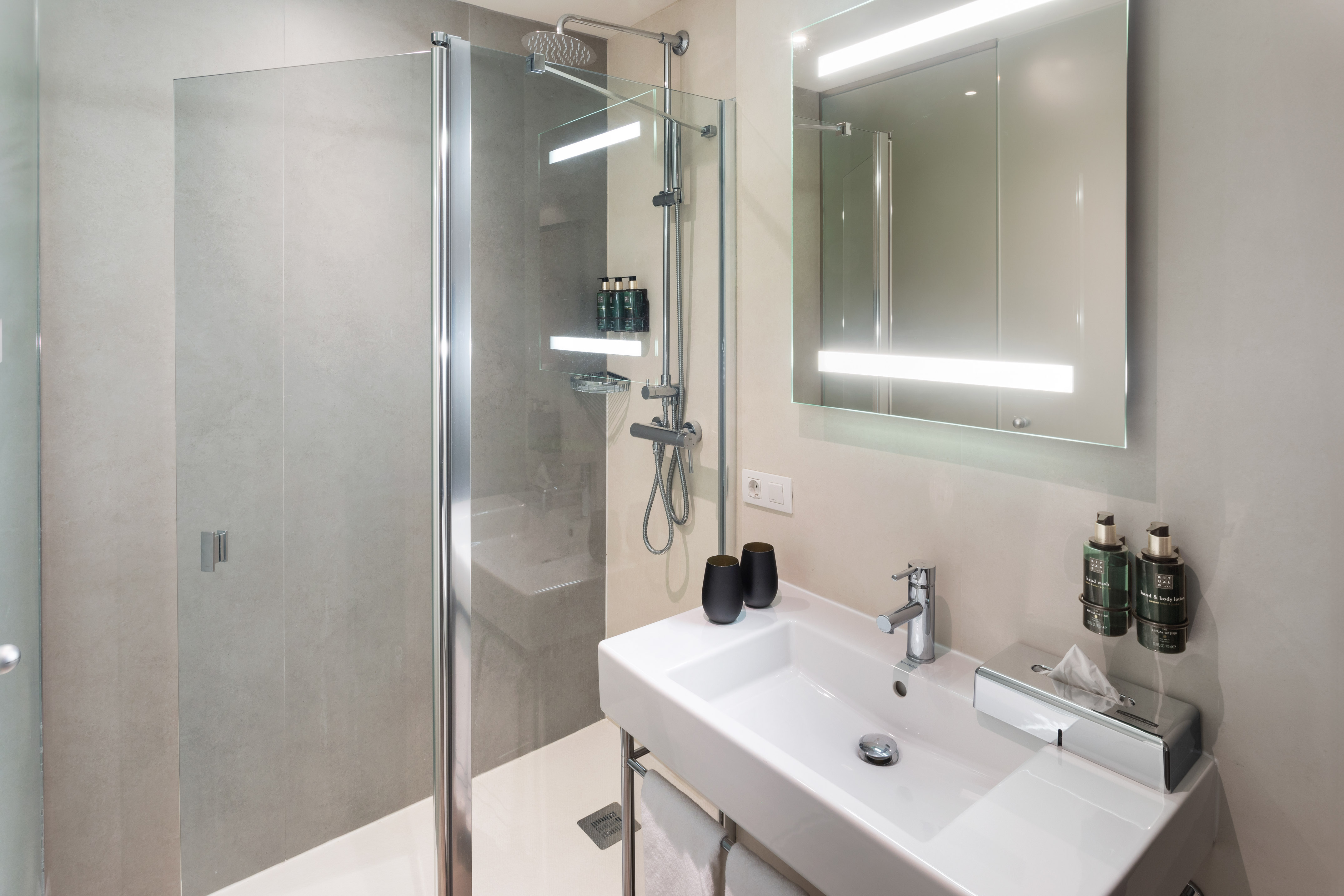 Modern hotel bathroom with a glass shower cabin, white sink, and LED-lit mirror.