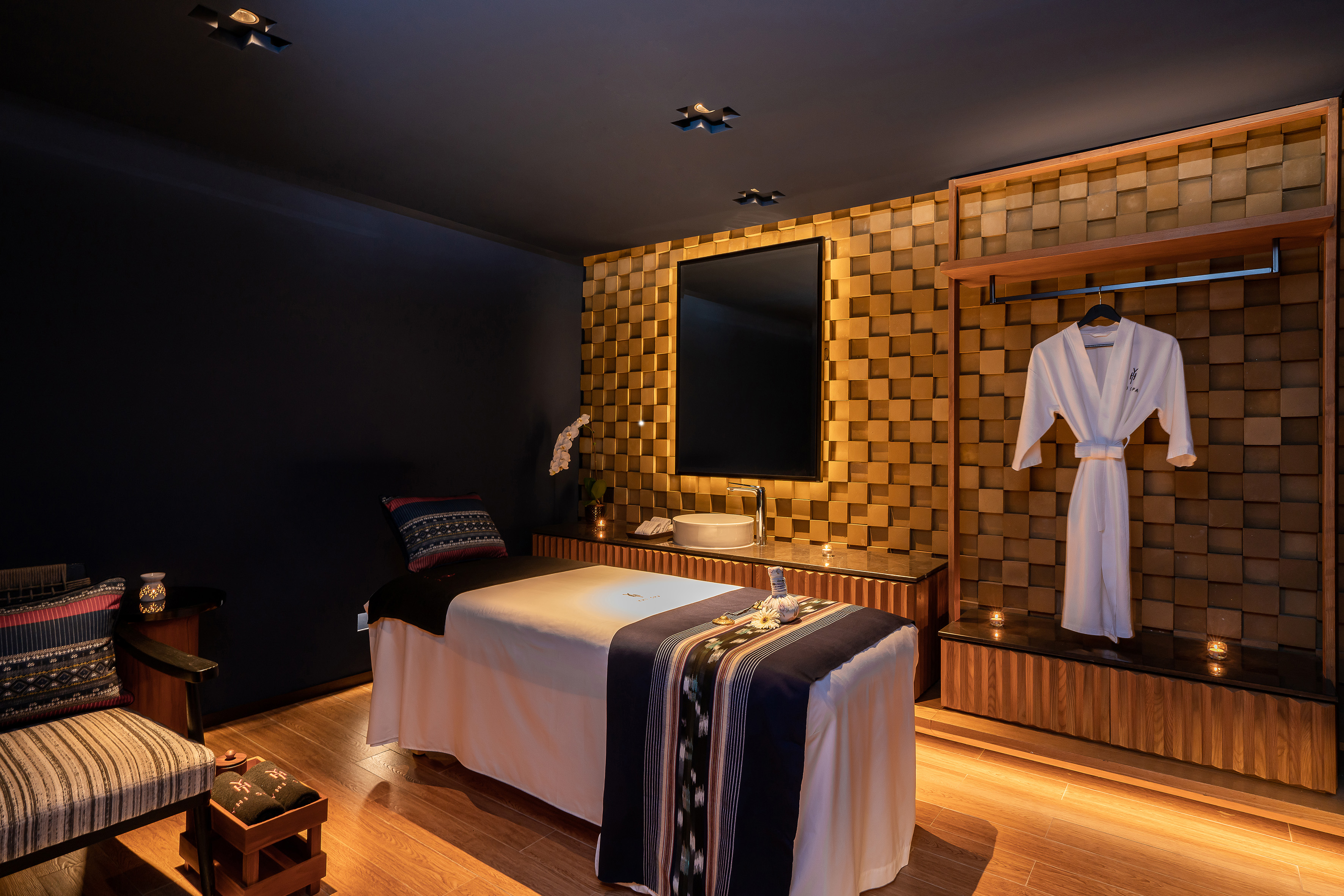 Luxurious spa treatment room with massage bed, gold wall, and wellness amenities.