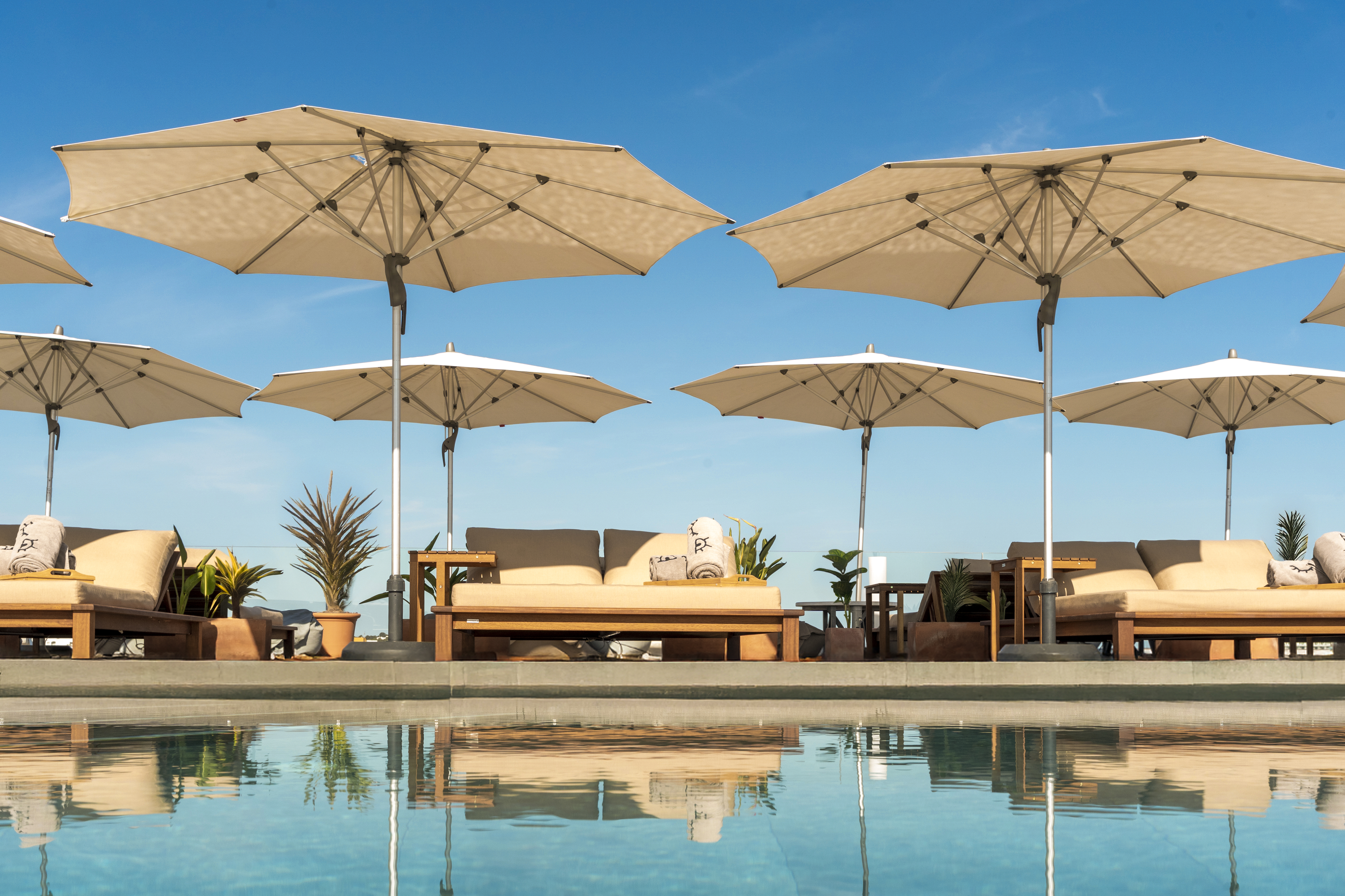 Luxurious pool deck with beige umbrellas, lounge chairs, and sparkling blue water.