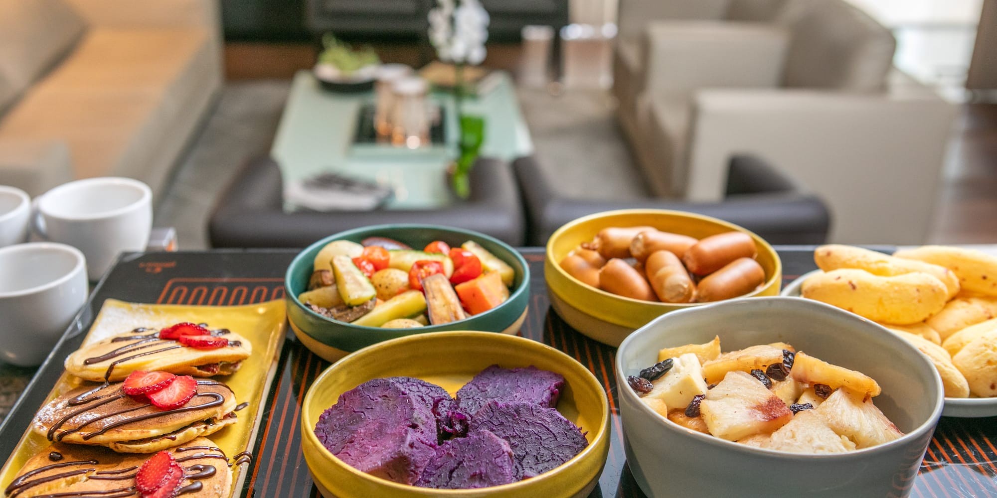 Breakfast platter with pancakes, sausages, roasted vegetables, and purple yams.