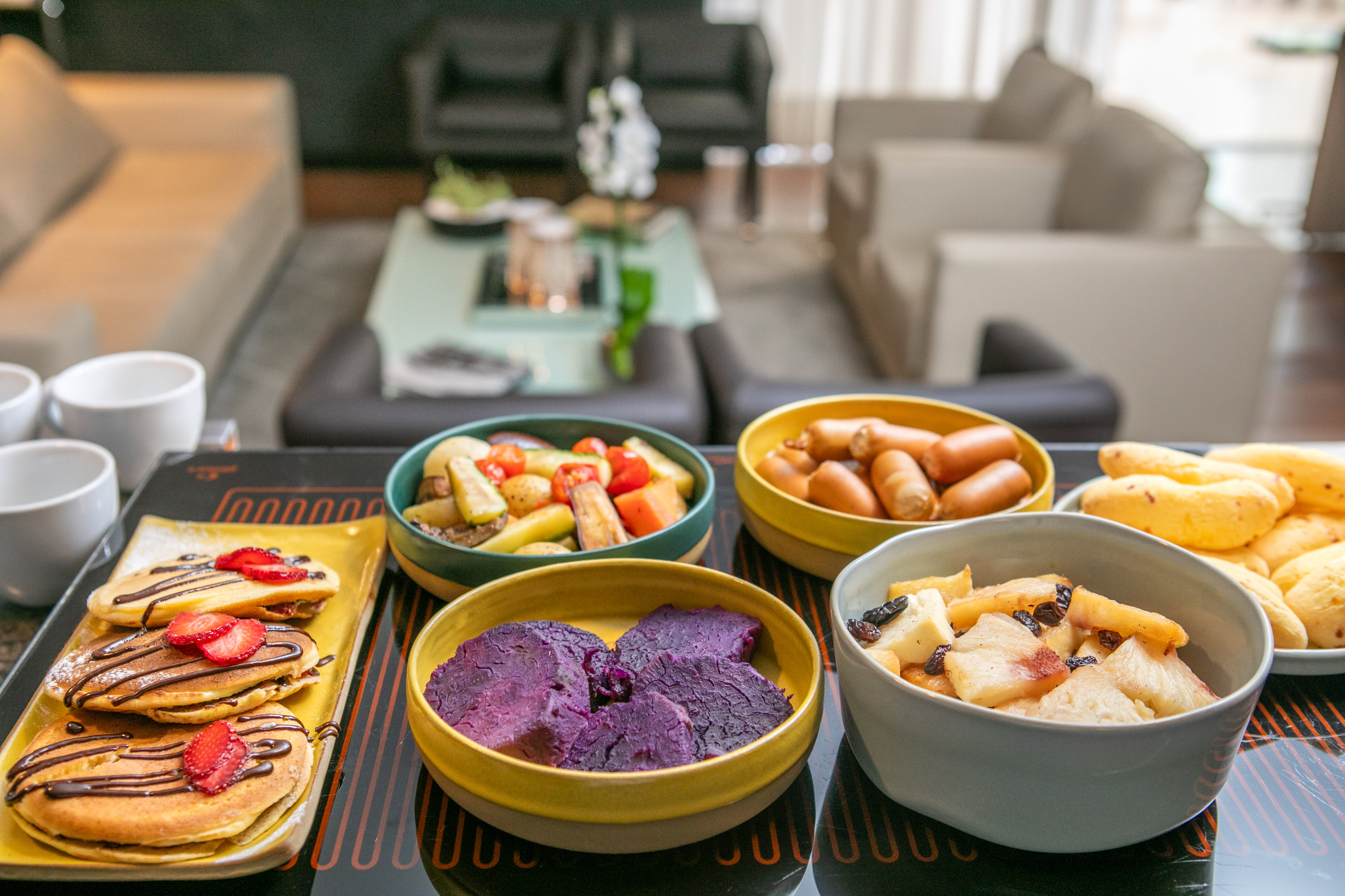 Breakfast platter with pancakes, sausages, roasted vegetables, and purple yams.