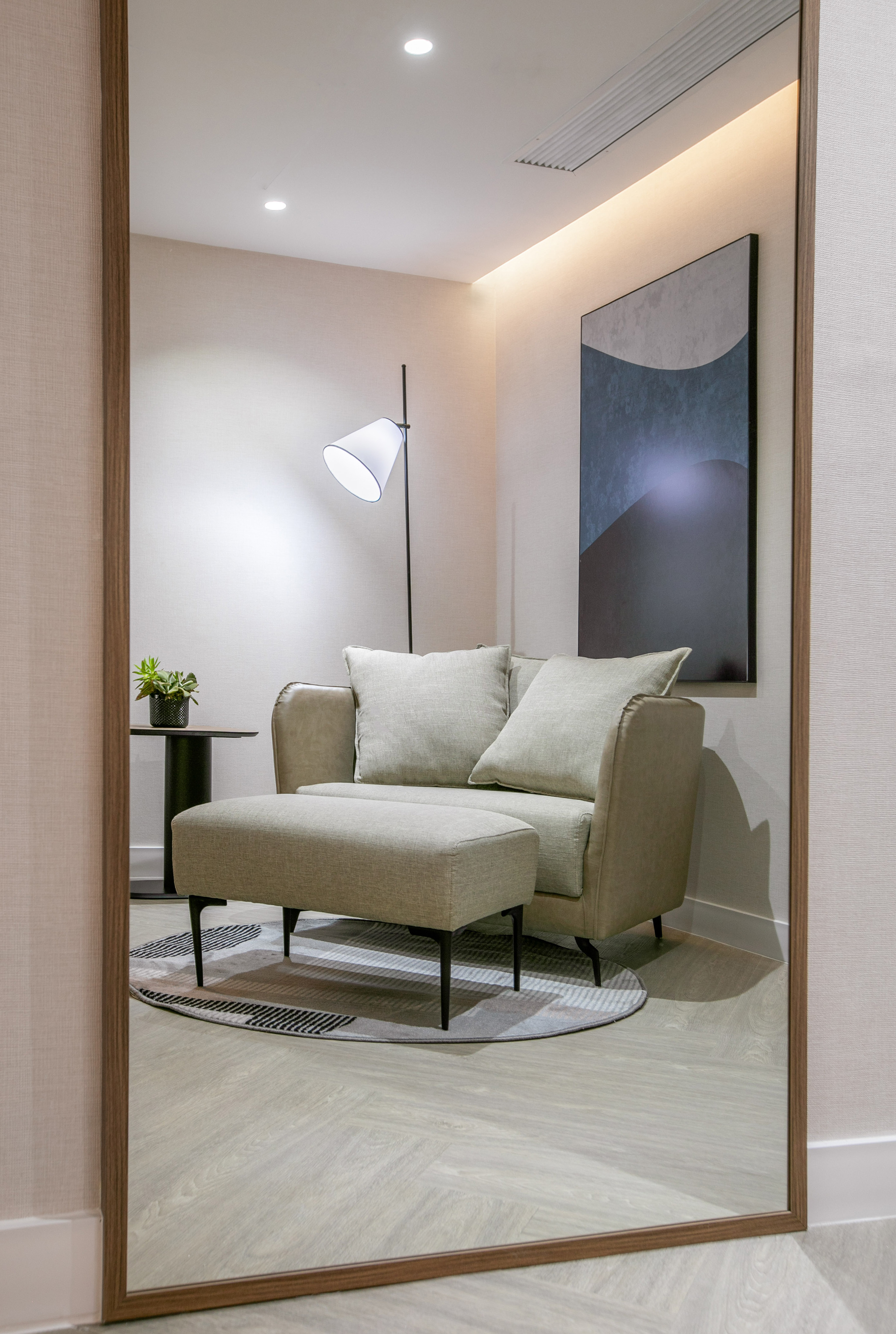 Modern lounge chair, ottoman, floor lamp, and abstract art reflected in a mirror.
