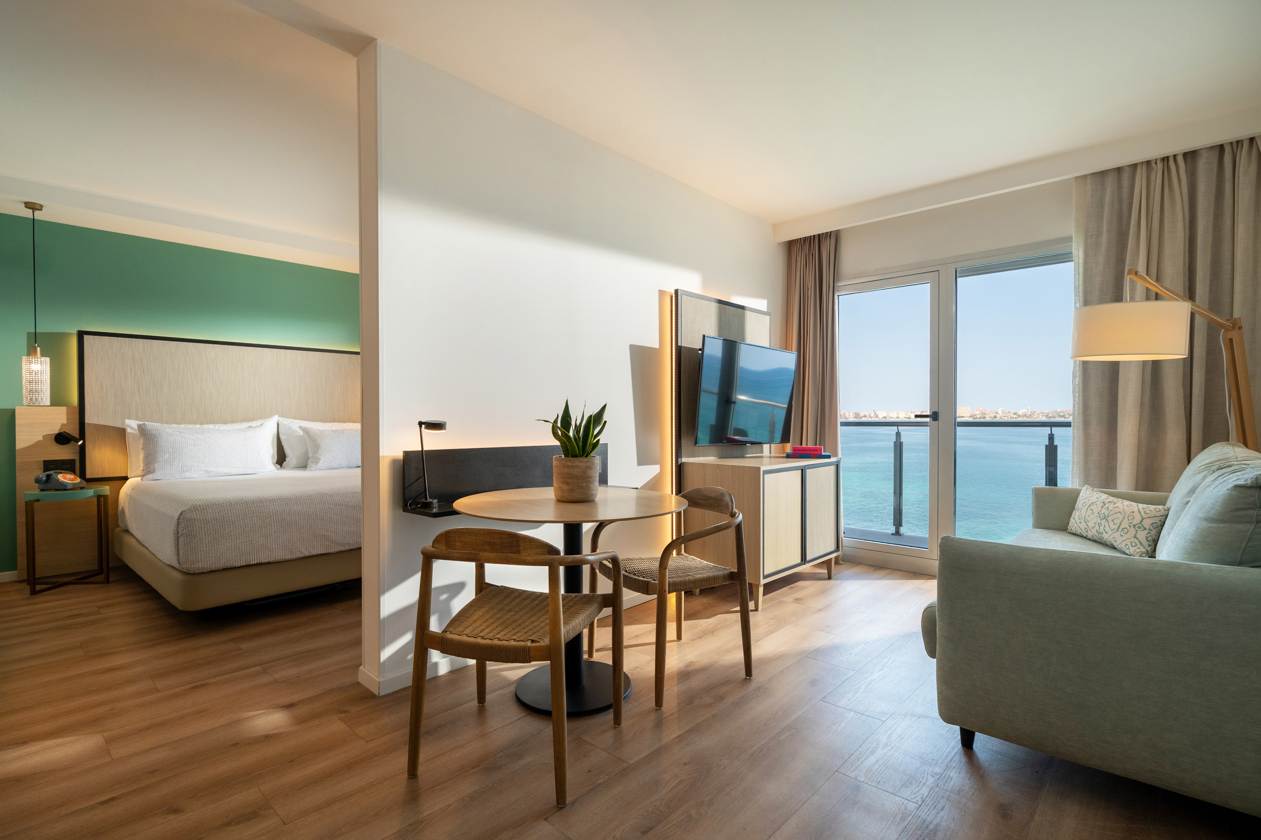 Bright hotel suite with separate bedroom, living area, and expansive sea view.