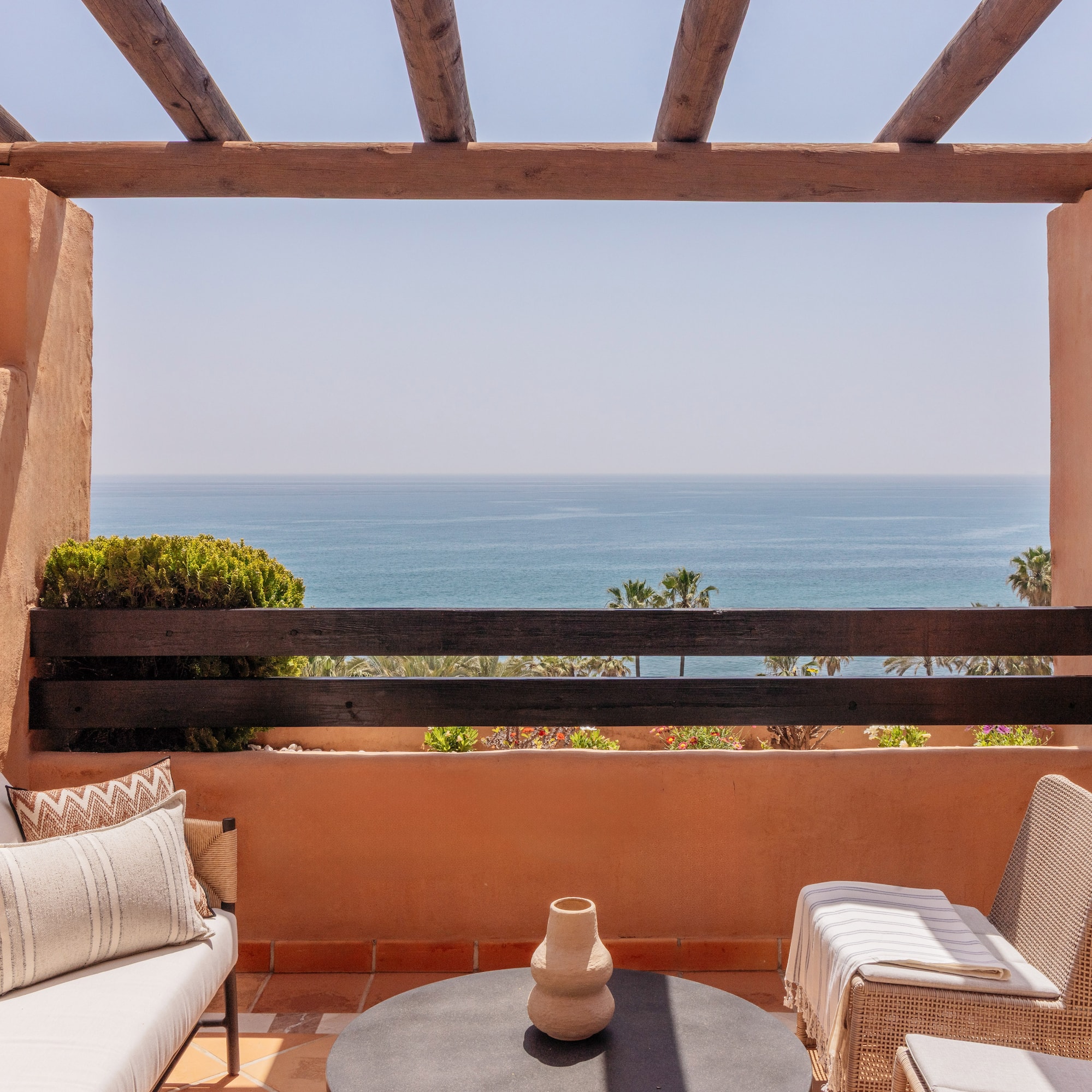 Mediterranean balcony with sea view, terracotta walls, and outdoor furniture.