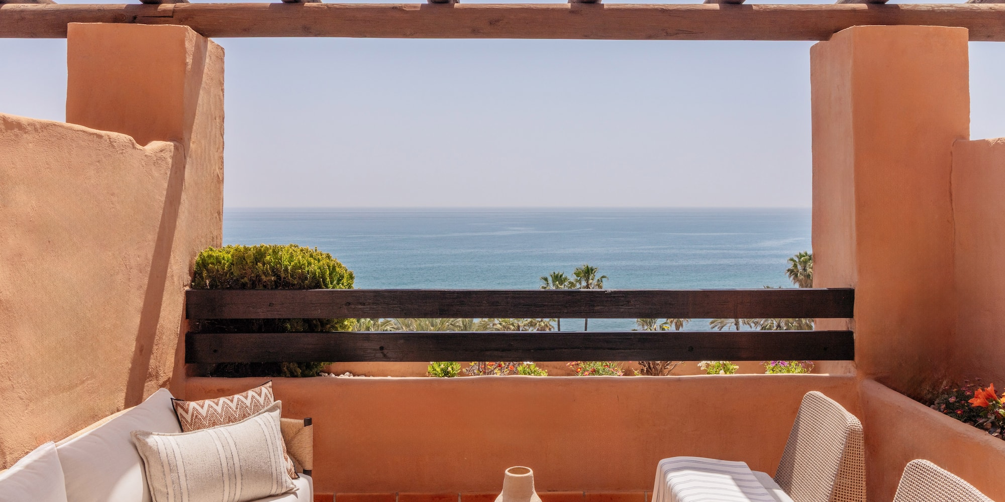 Mediterranean balcony with sea view, terracotta walls, and outdoor furniture.