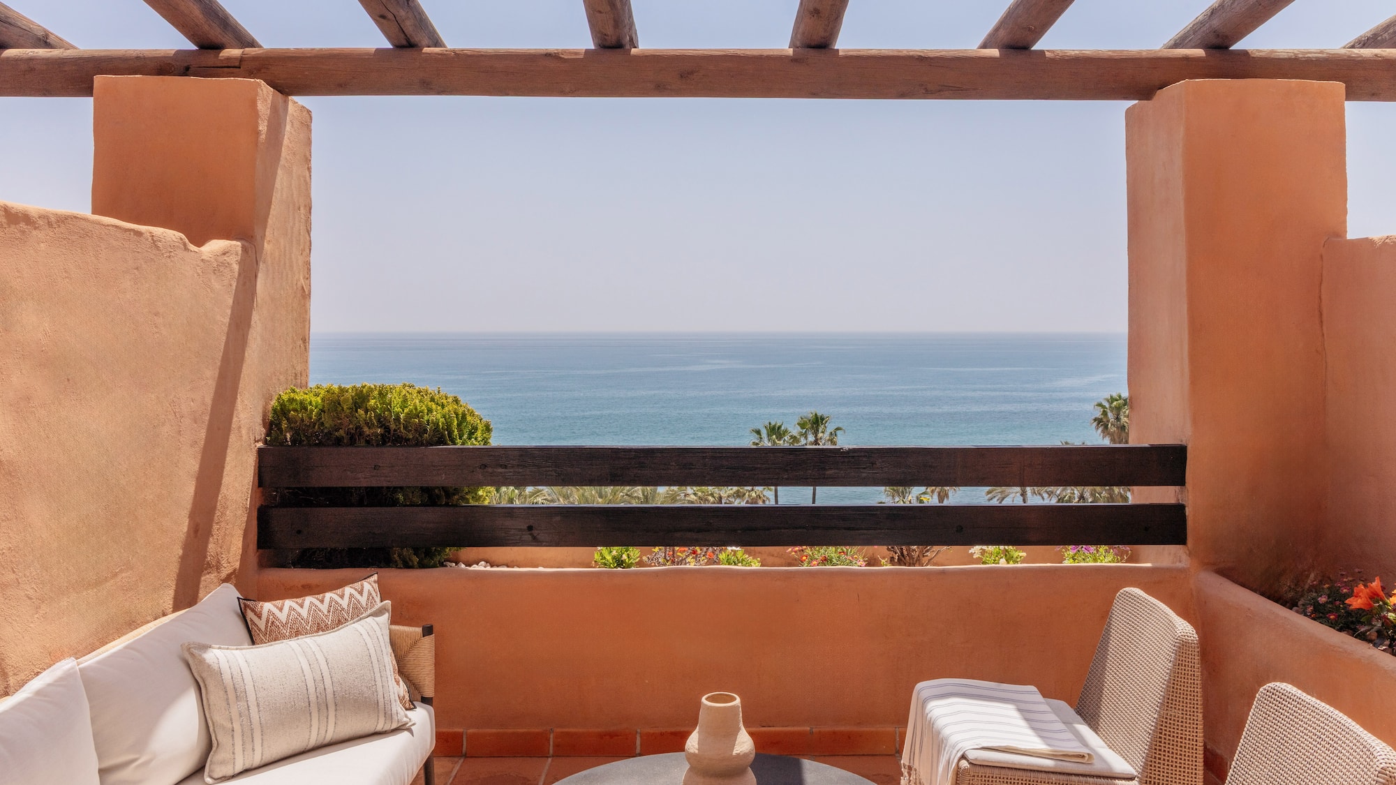 Mediterranean balcony with sea view, terracotta walls, and outdoor furniture.