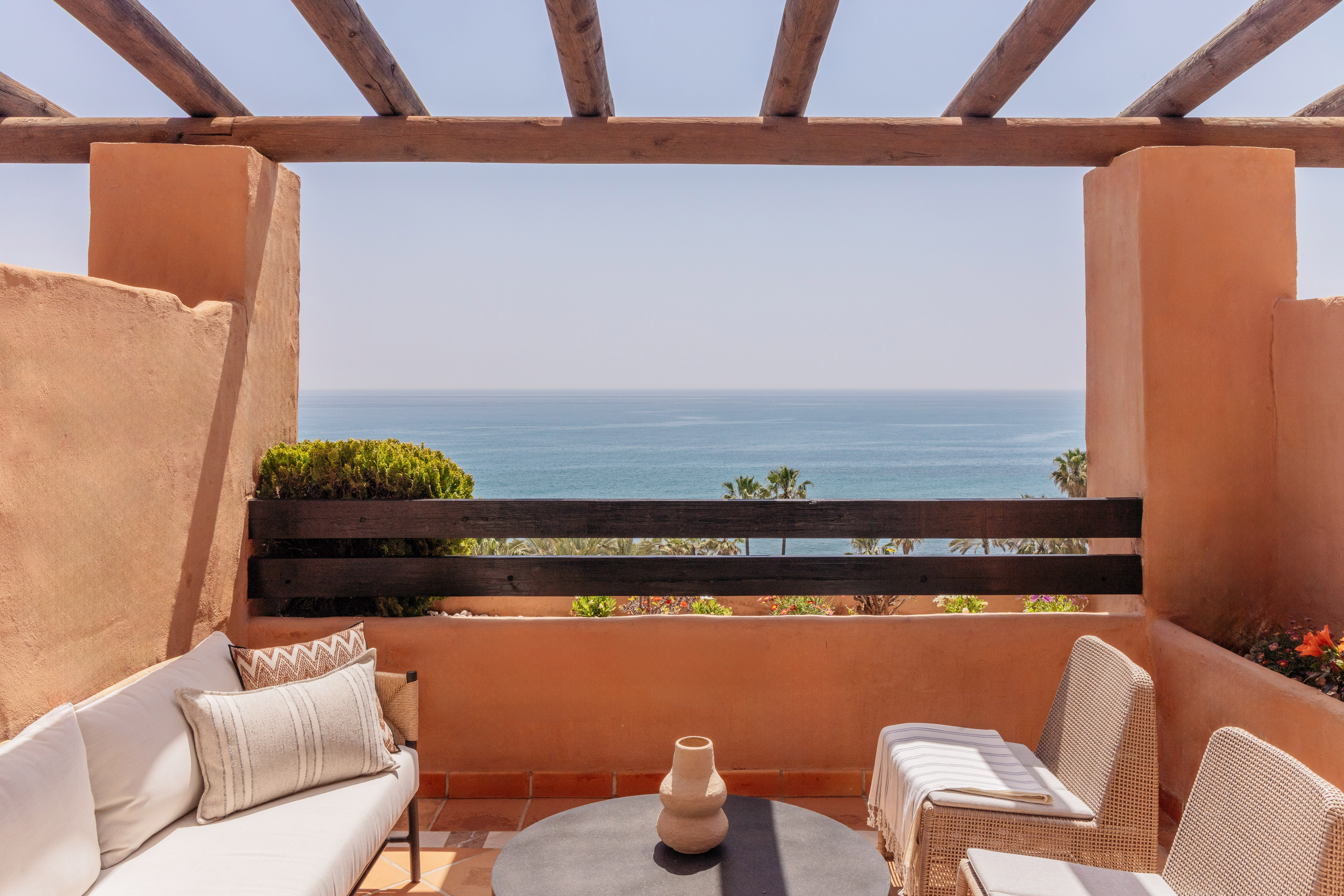 Mediterranean balcony with sea view, terracotta walls, and outdoor furniture.