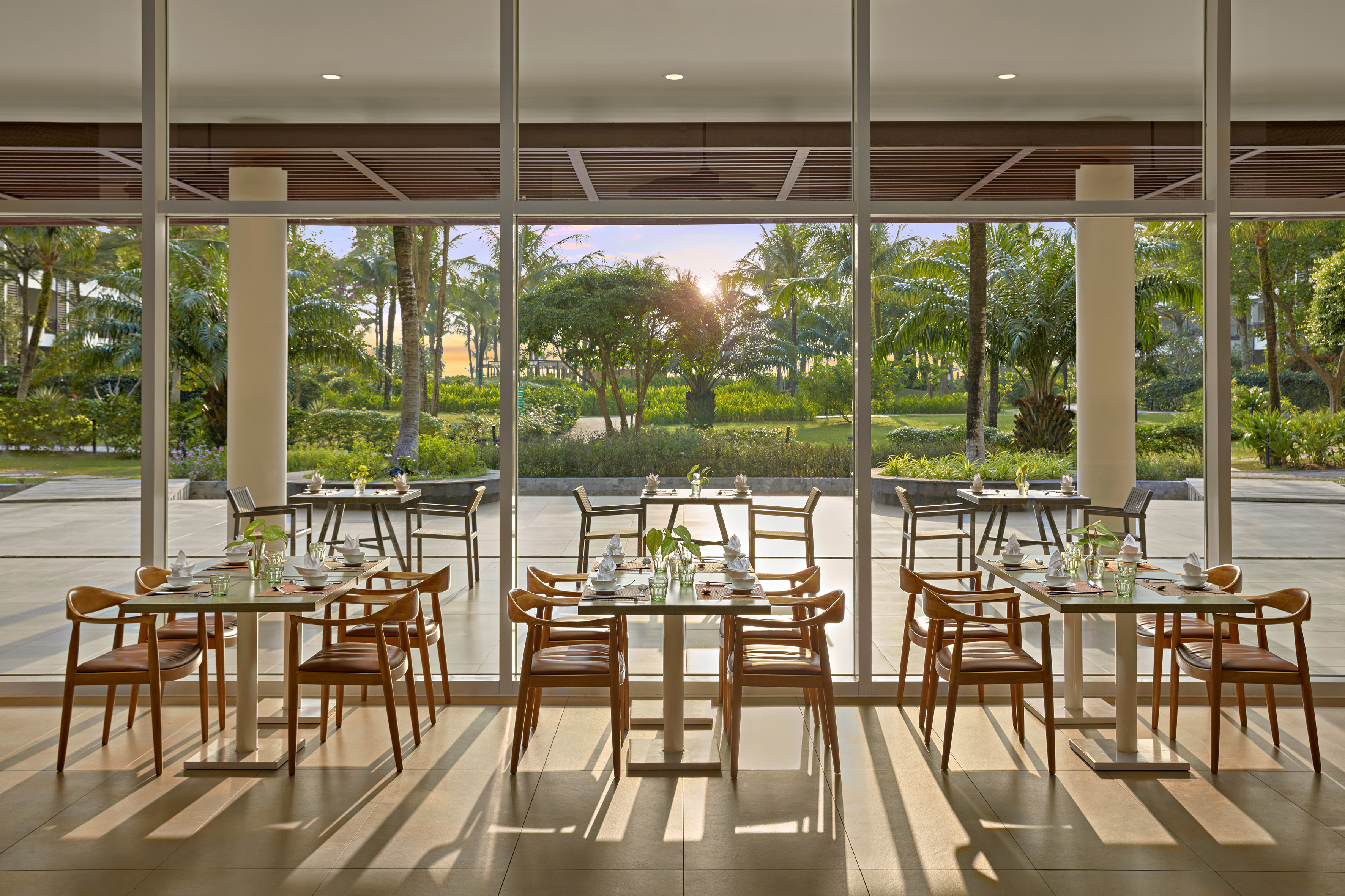 Resort restaurant with tropical garden view, set tables, and golden hour light.