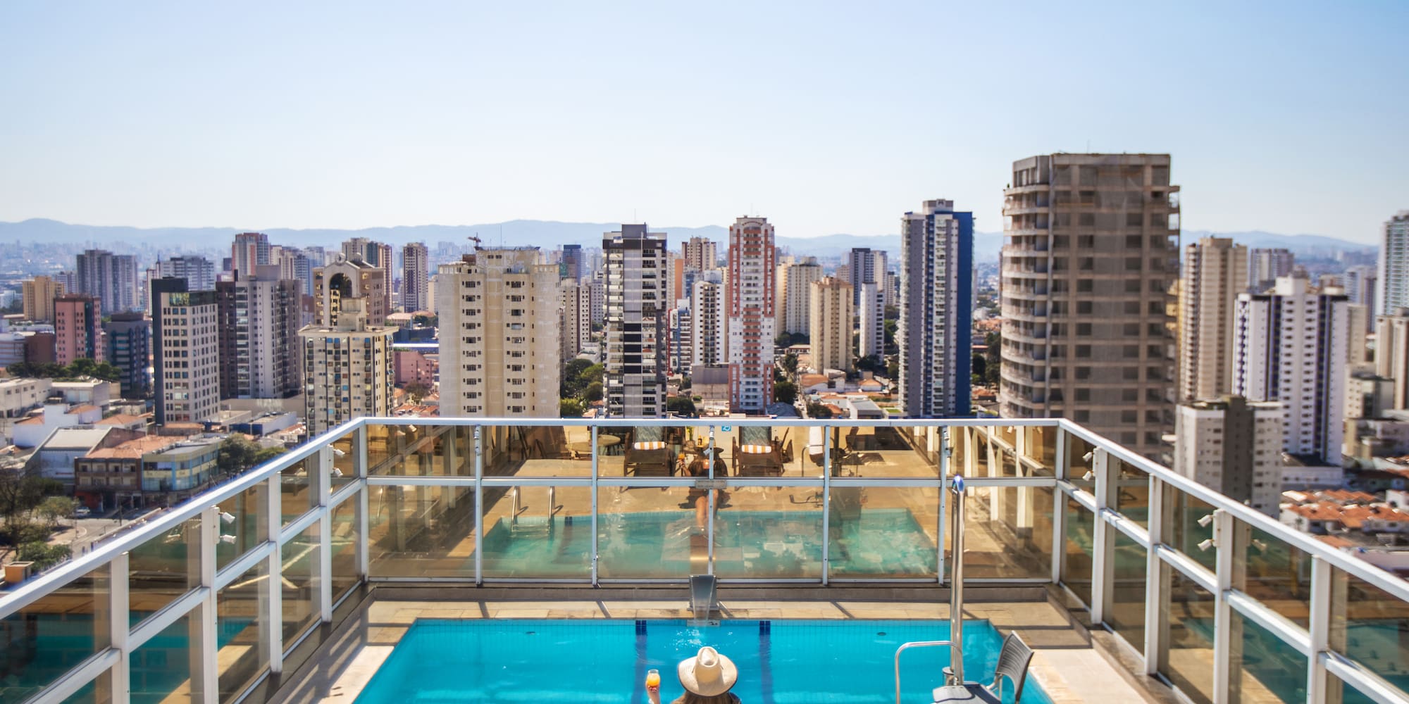 a woman sitting on a rooftop with a pool and a city in the background