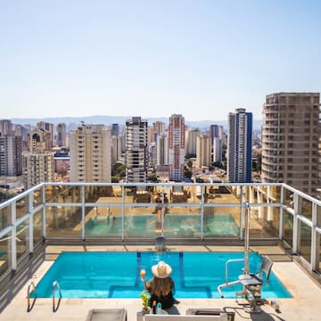 a woman sitting on a rooftop with a pool and a city in the background