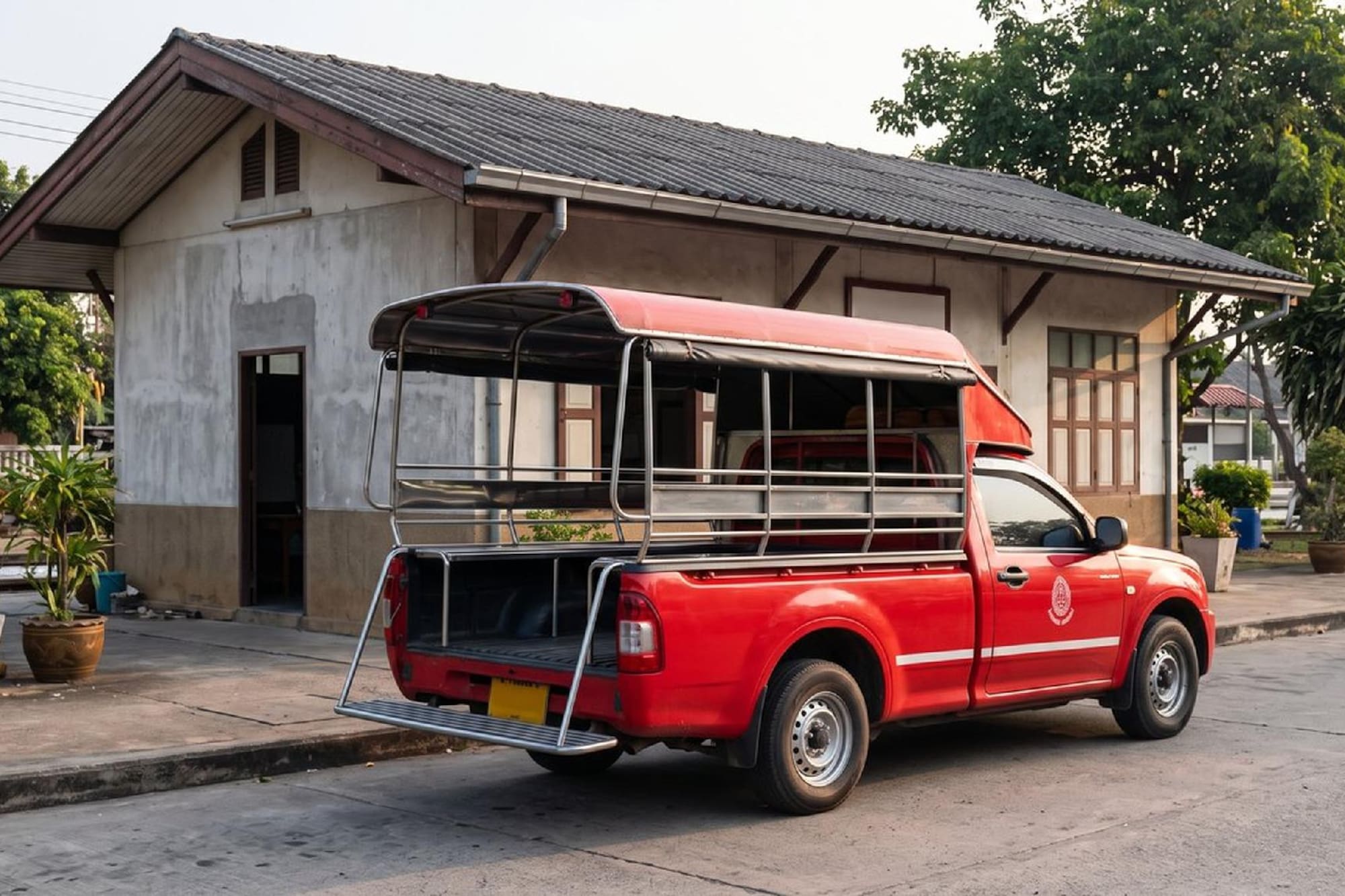 Red songthaew pickup truck parked outside a traditional Thai building.