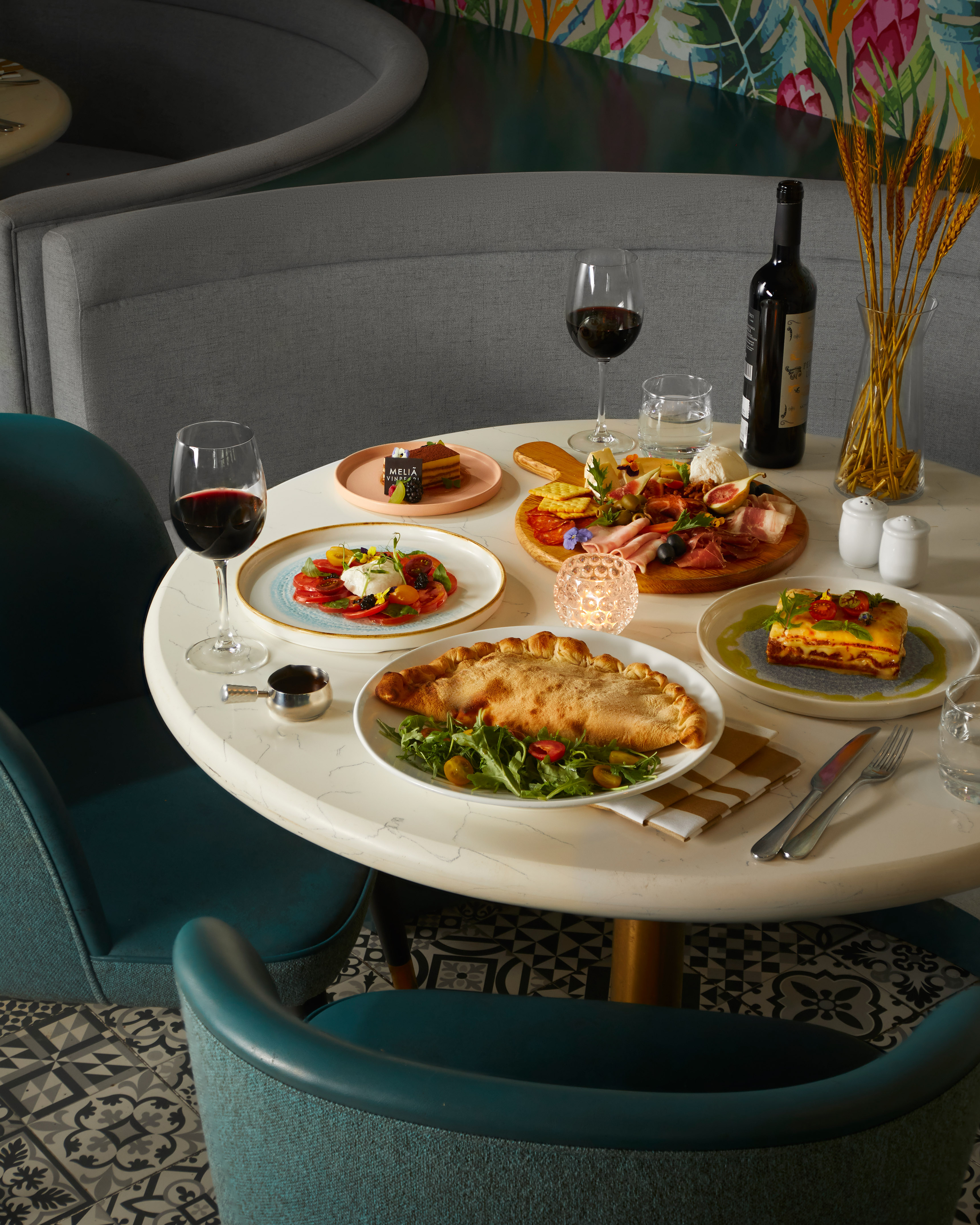 Italian restaurant table with lasagna, calzone, charcuterie, wine, dessert.