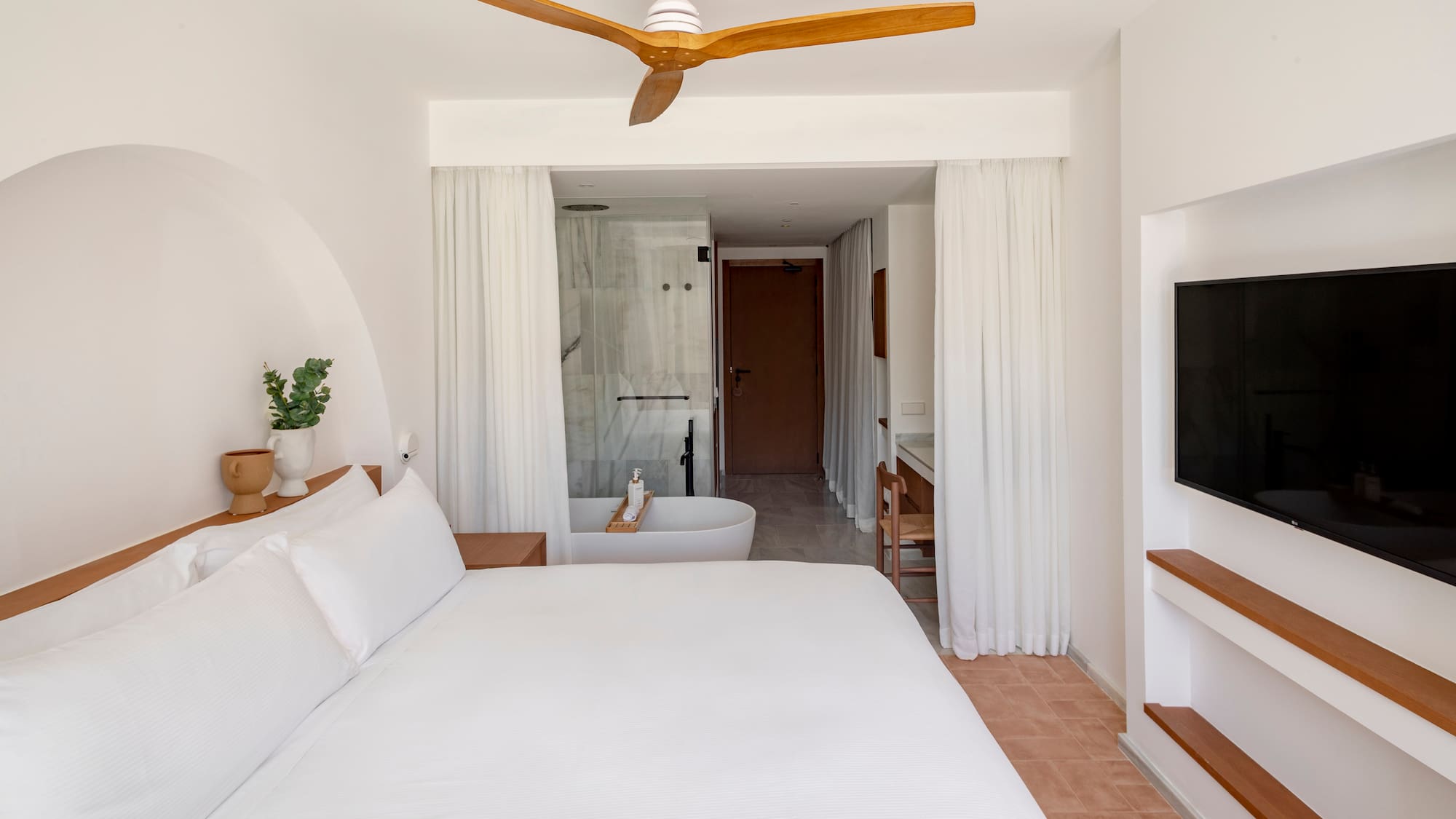a white bed with a white ceiling fan and a bathtub