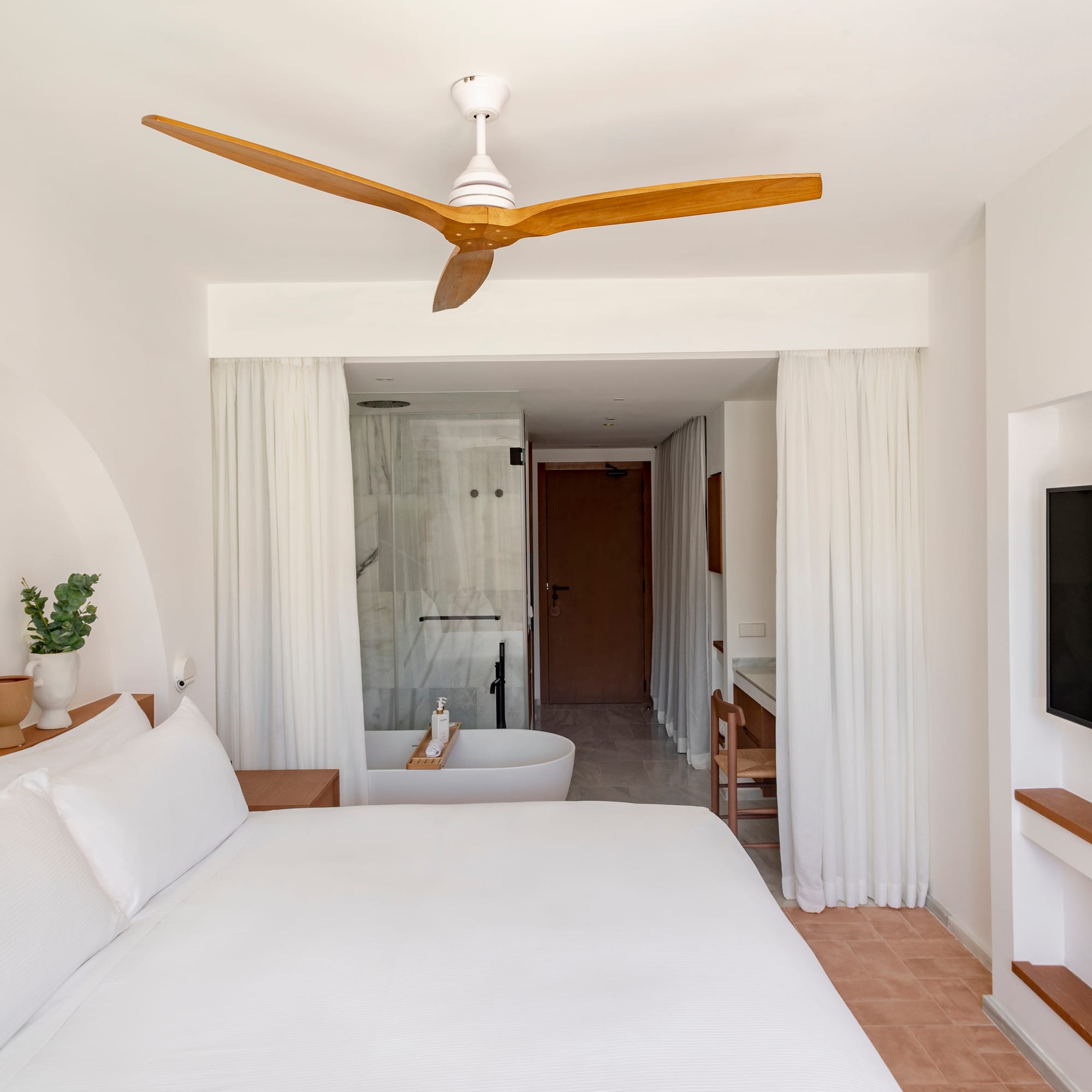a white bed with a white ceiling fan and a bathtub