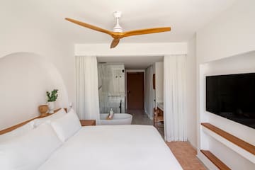 a white bed with a white ceiling fan and a bathtub