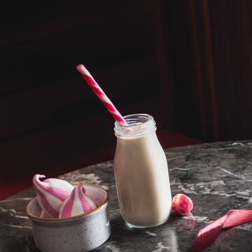 a glass bottle with a straw next to a bowl of meringues