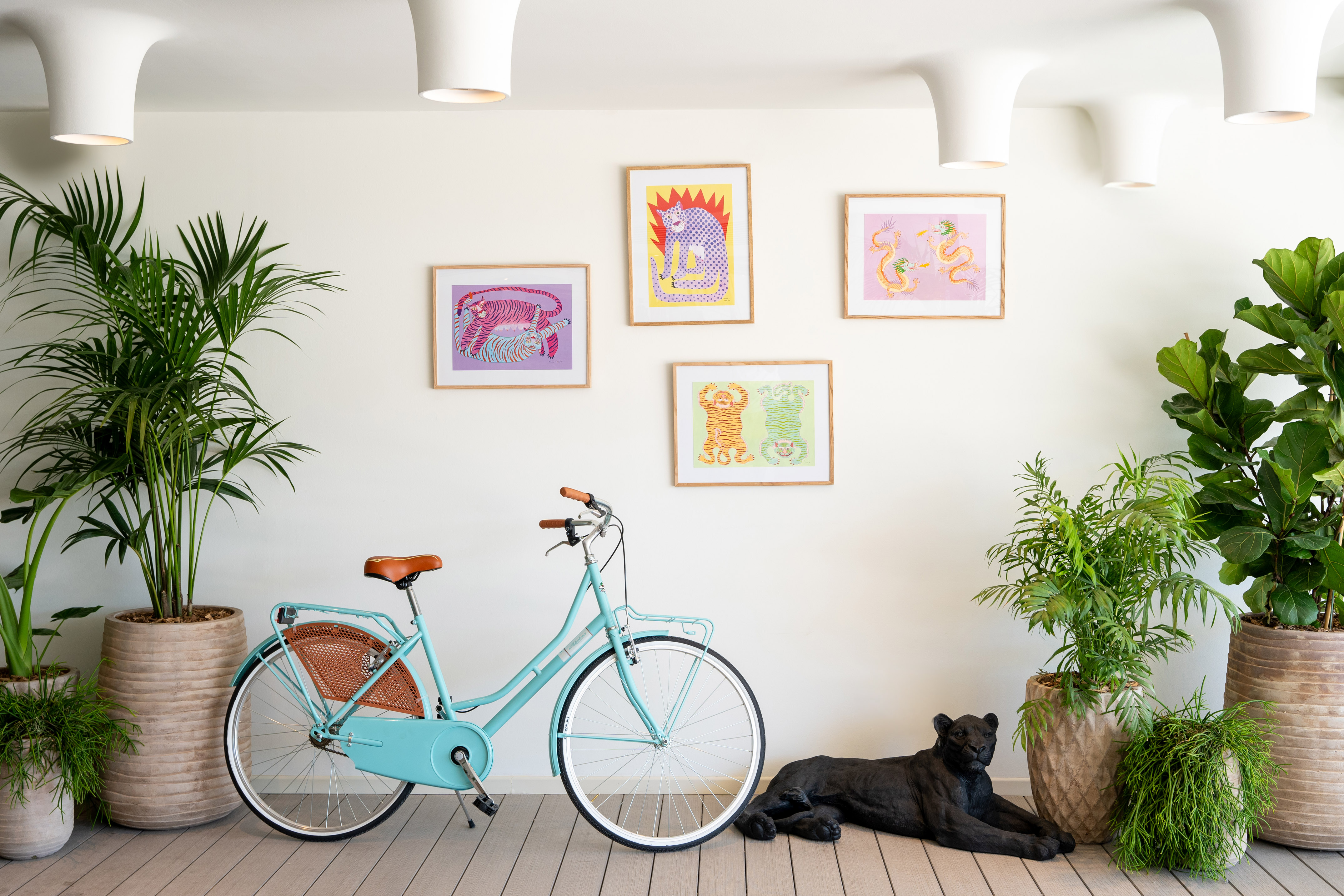 Vibrant animal art, blue bicycle, large potted plants, black panther sculpture, modern decor.