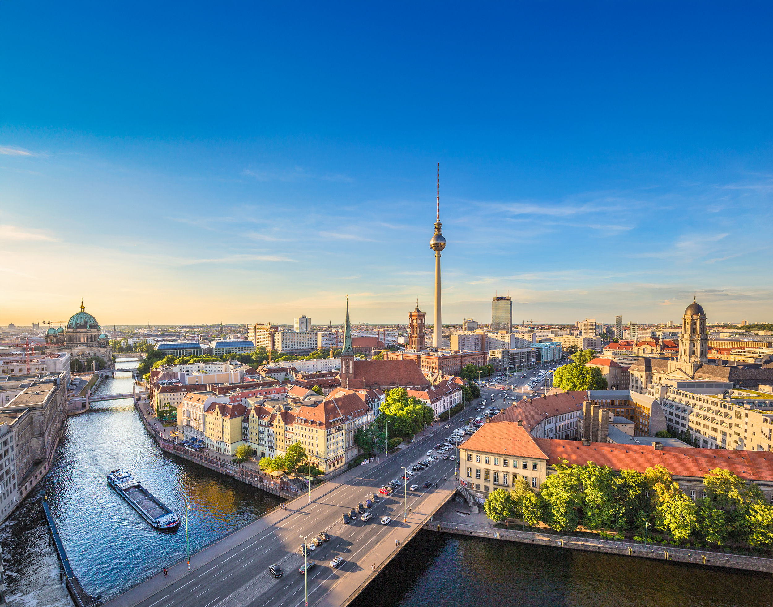 Aerial Berlin cityscape with Spree River, Cathedral, TV Tower, roads at golden hour.