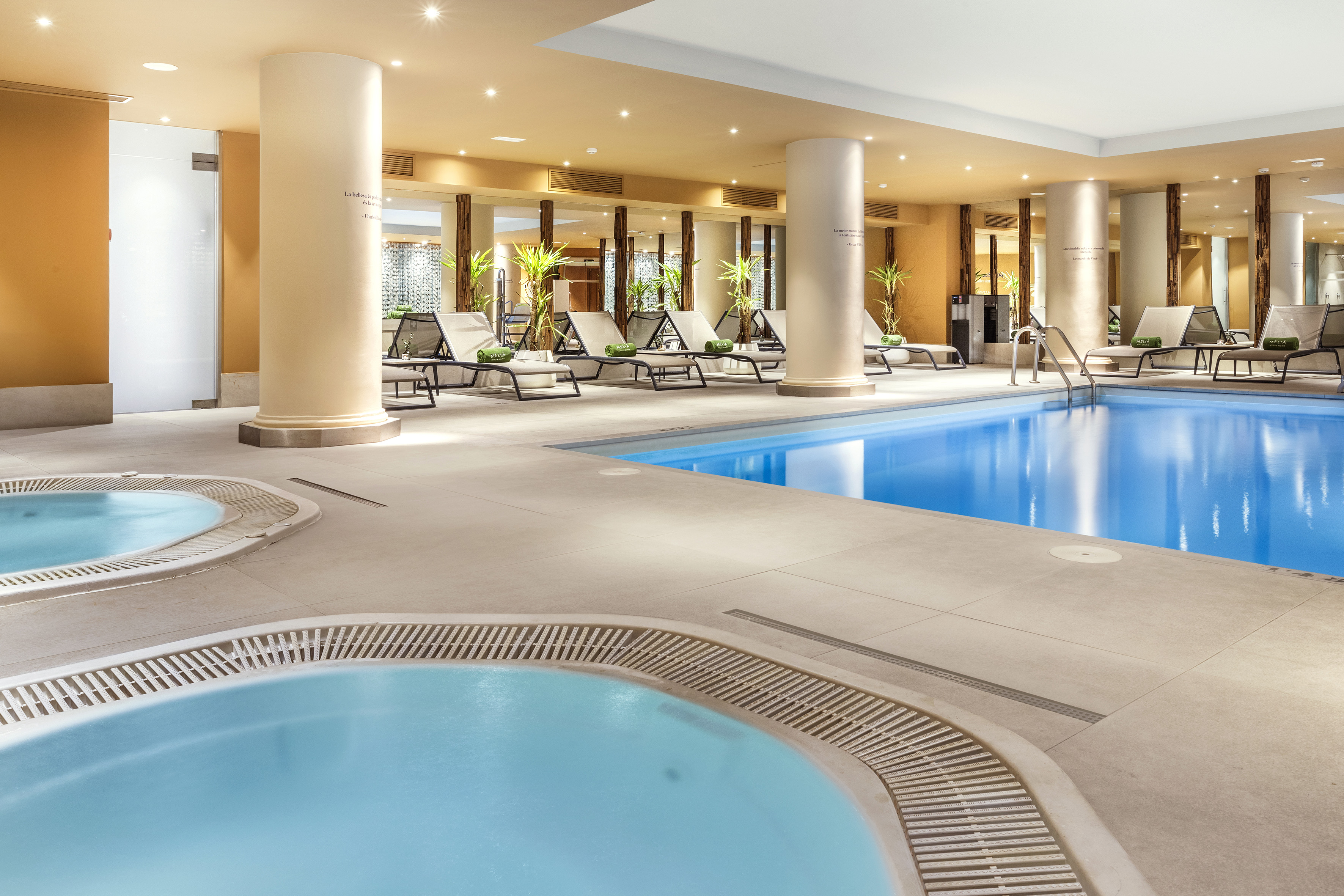 Indoor hotel spa with swimming pool, two hot tubs, and lounge chairs.