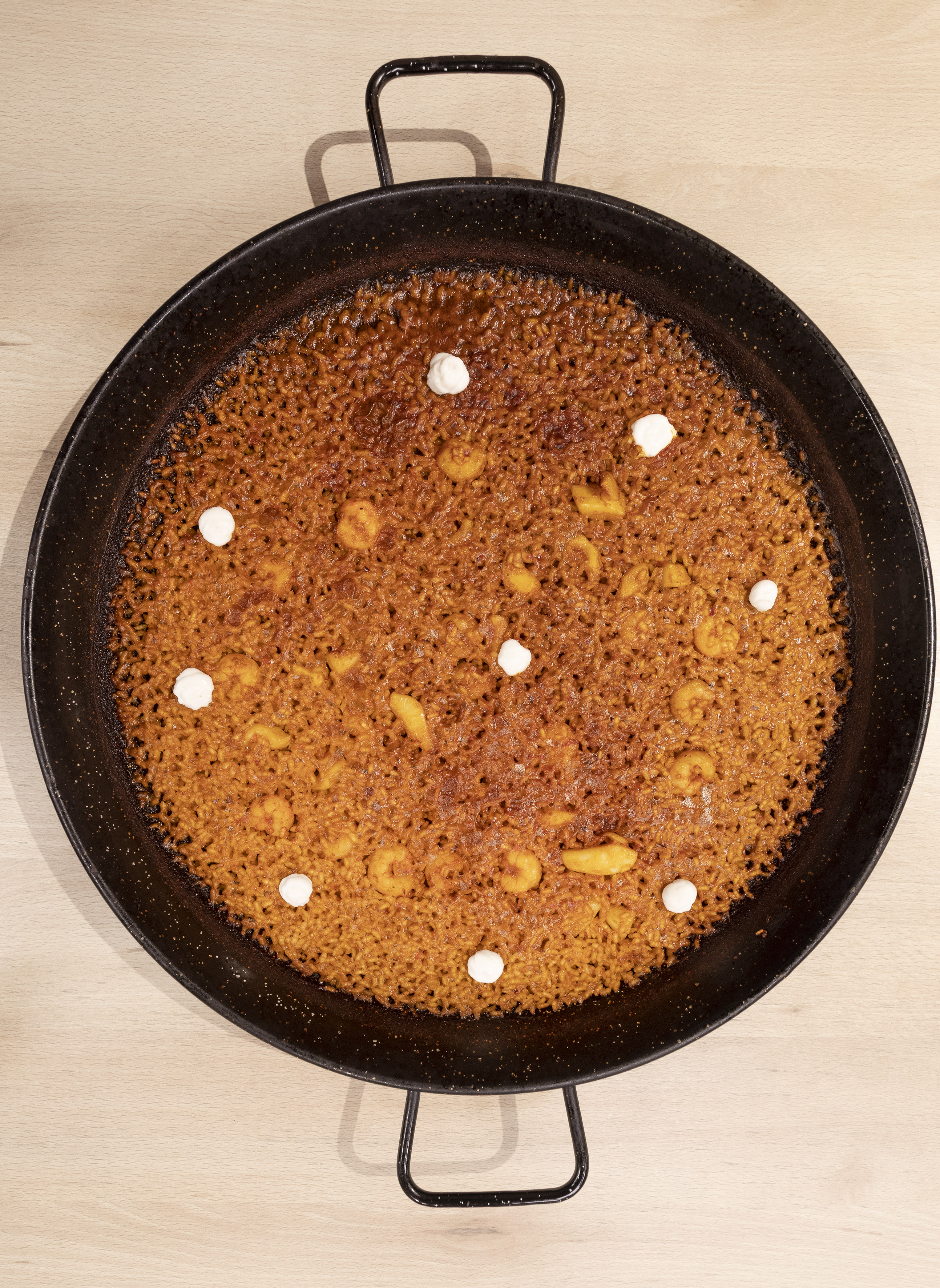 Golden seafood paella with prawns and aioli dots in a black paella pan.