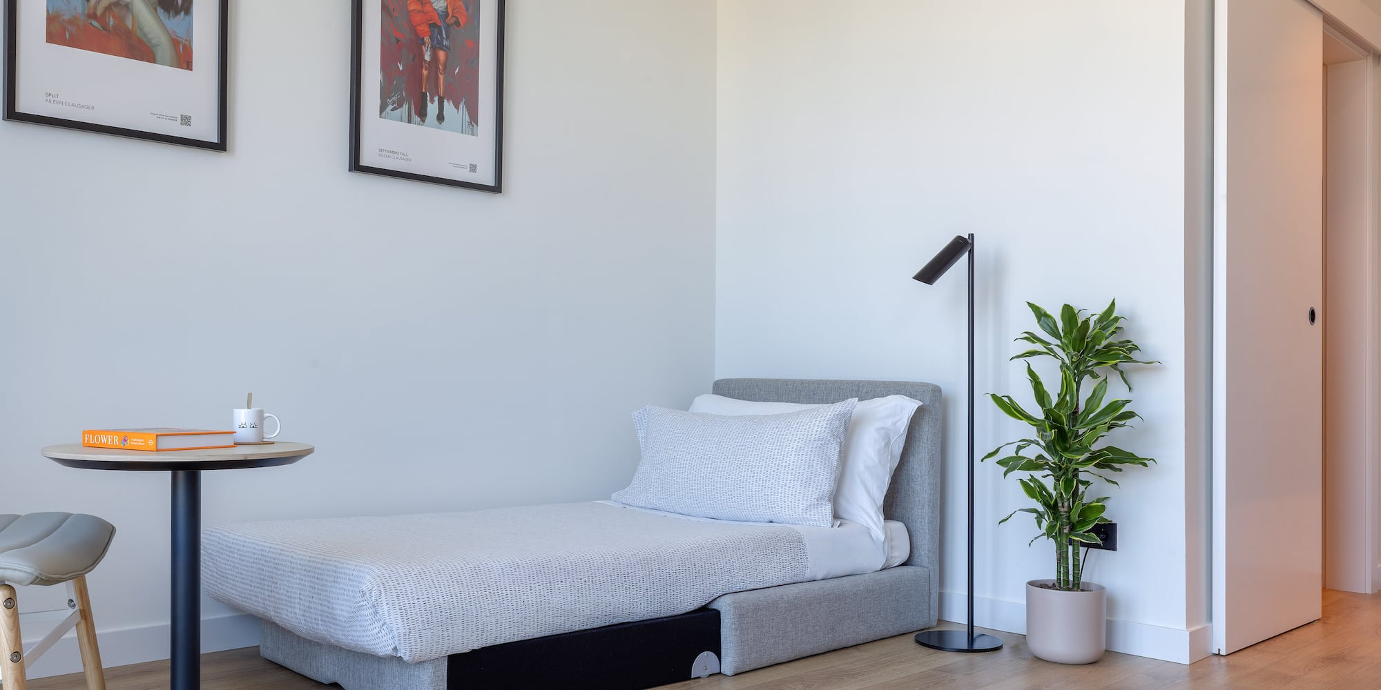 Estancia moderna con cama individual, mesa auxiliar, planta y arte en pared.