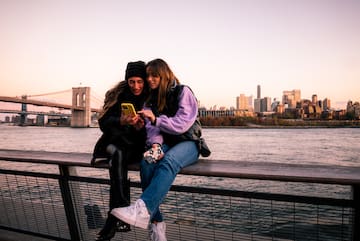 two women sitting on a railing looking at a phone