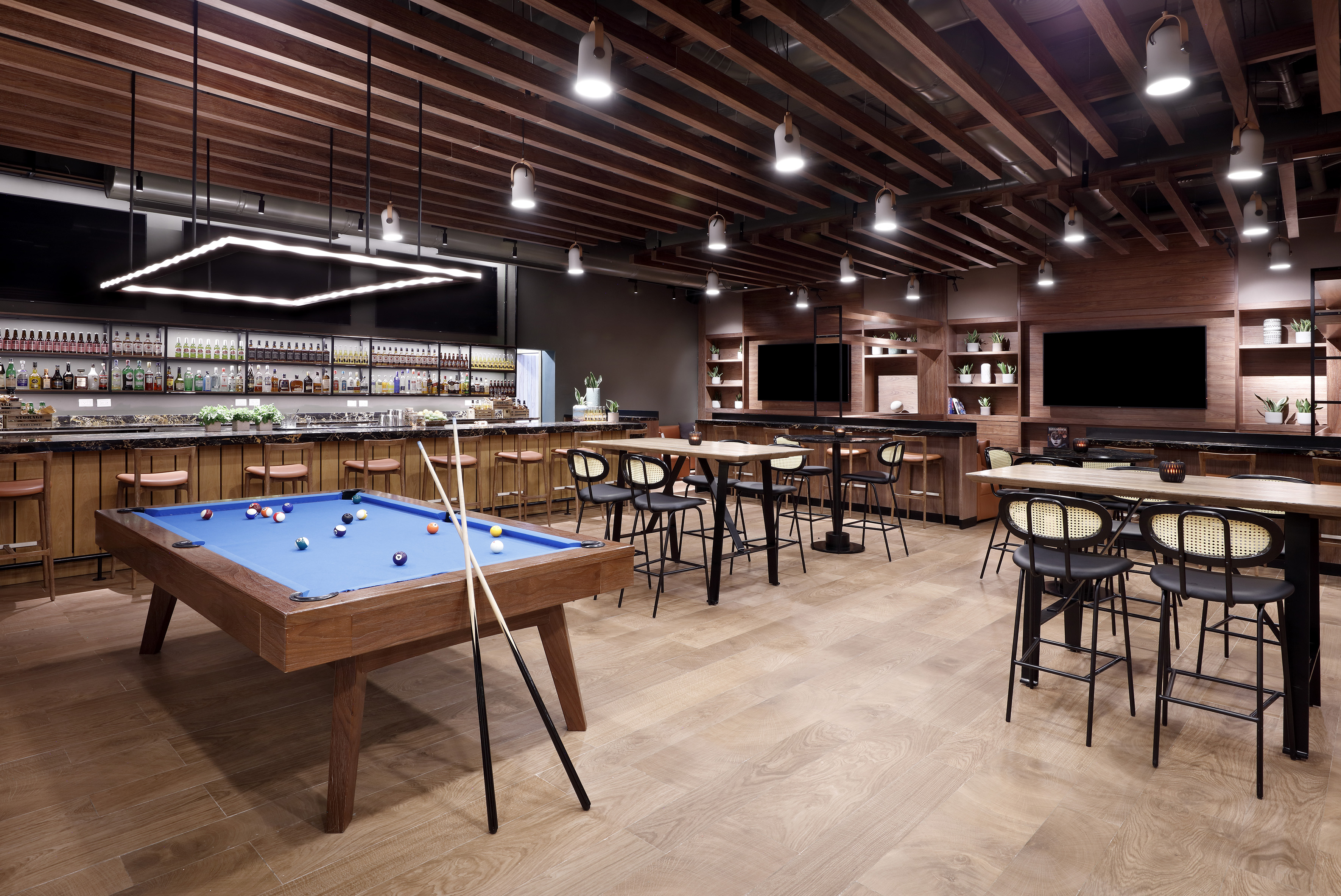 Modern lounge bar with blue pool table, stocked bar, and wood design.