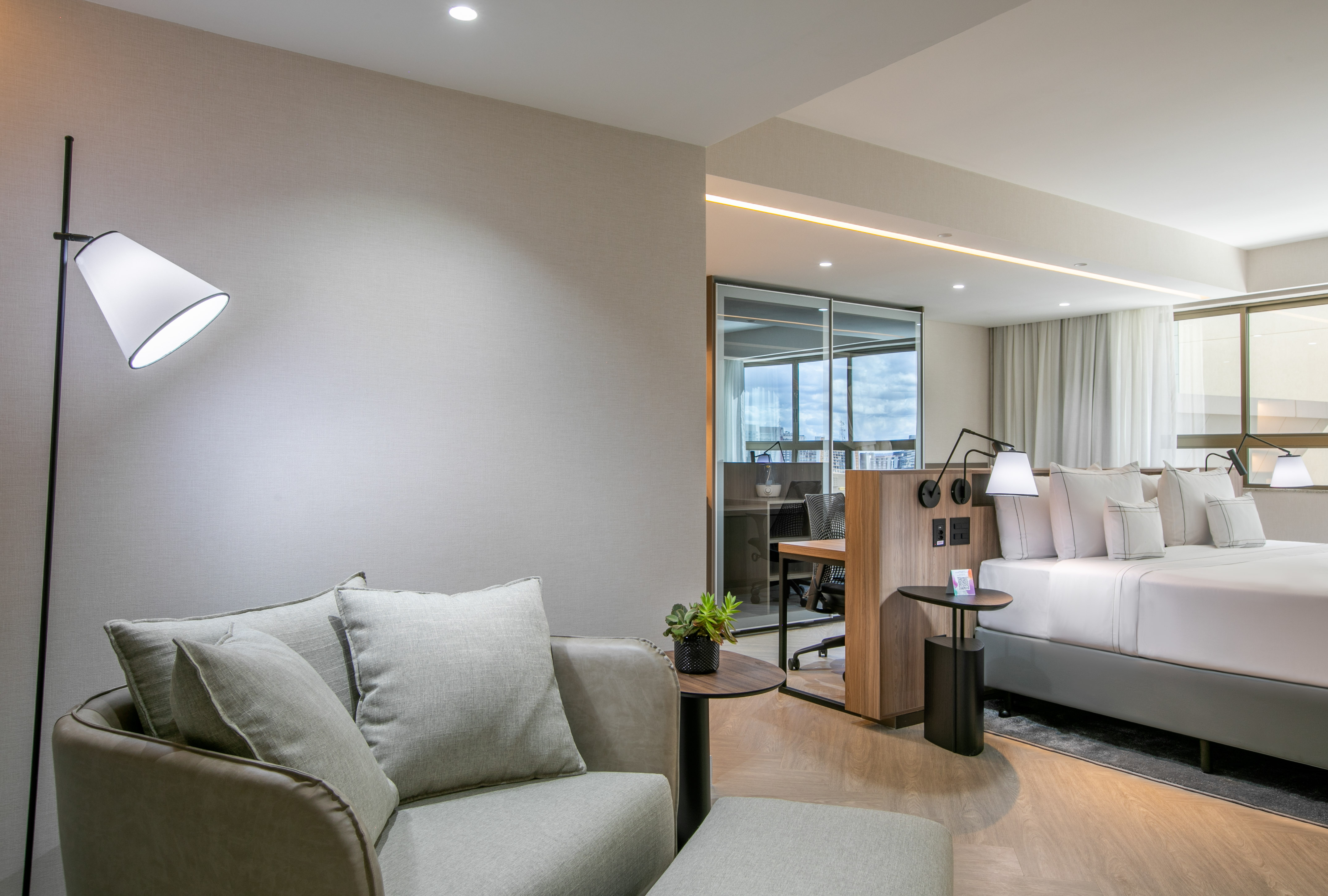 Modern hotel suite with living area, king bed, and desk workspace.