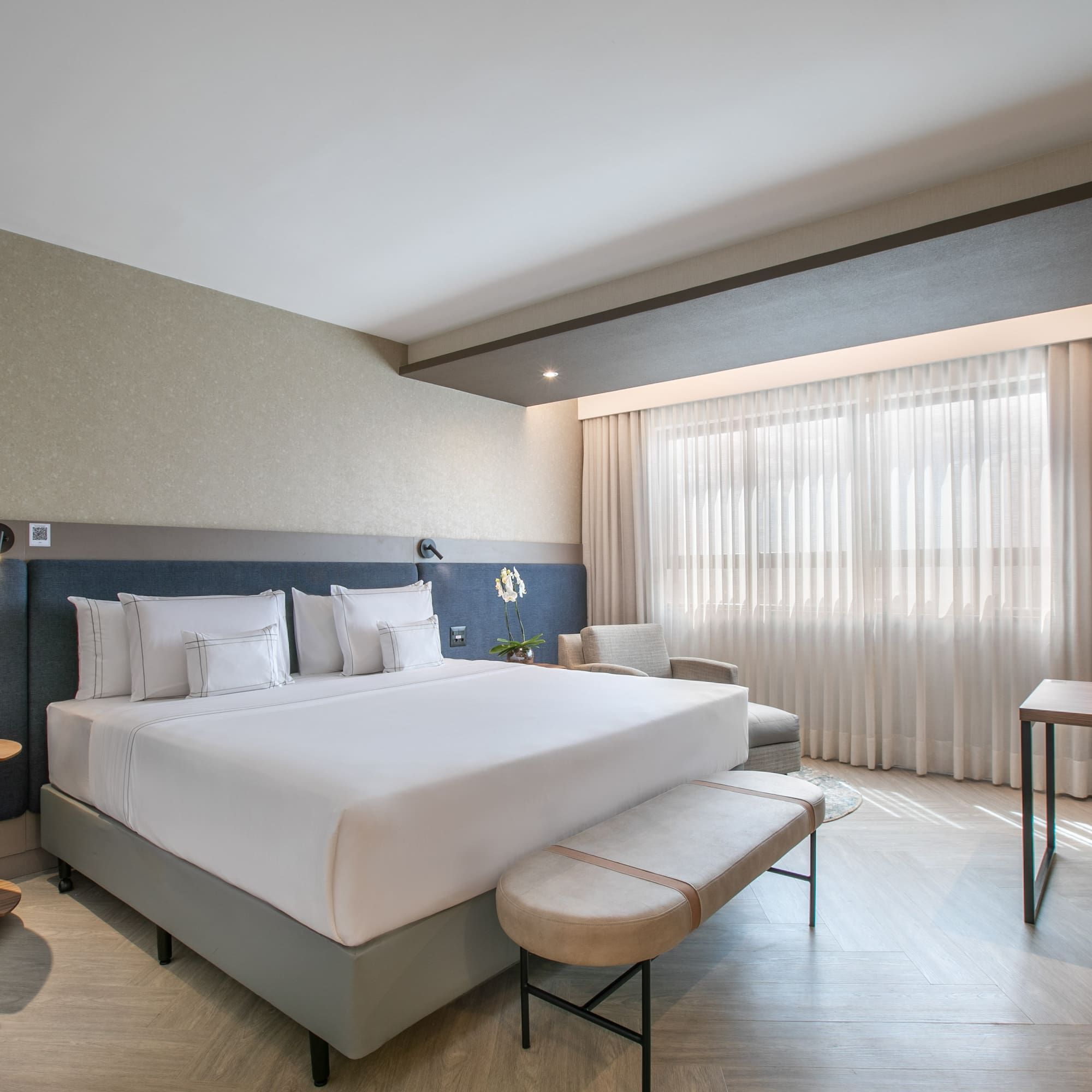 Modern hotel suite with king bed, dedicated workspace, and bright window.