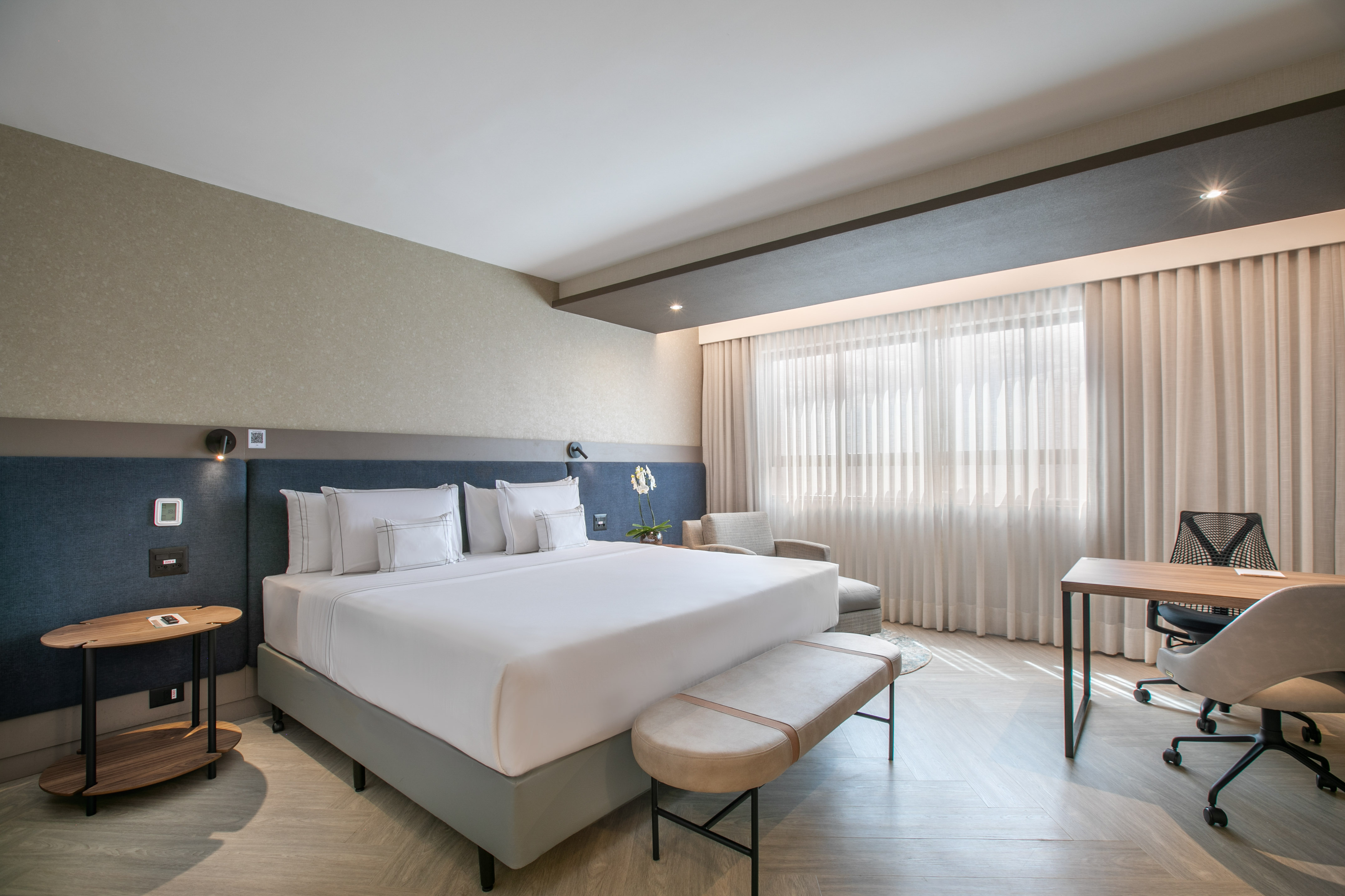 Modern hotel suite with king bed, dedicated workspace, and bright window.