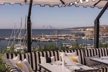 a table and chairs with a view of the water and boats in the background