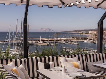 a table and chairs with a view of the water and boats in the background
