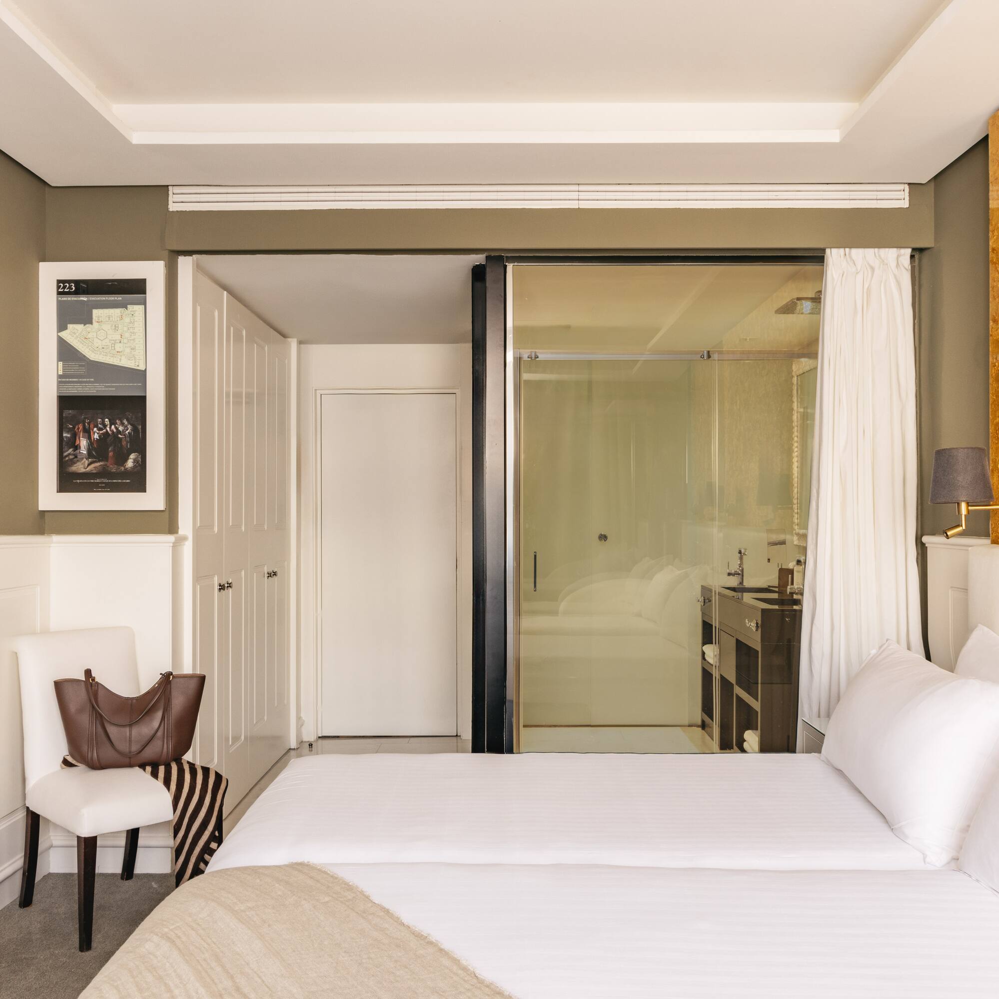 Modern hotel bedroom with twin beds, gold accent wall, and glass bathroom.