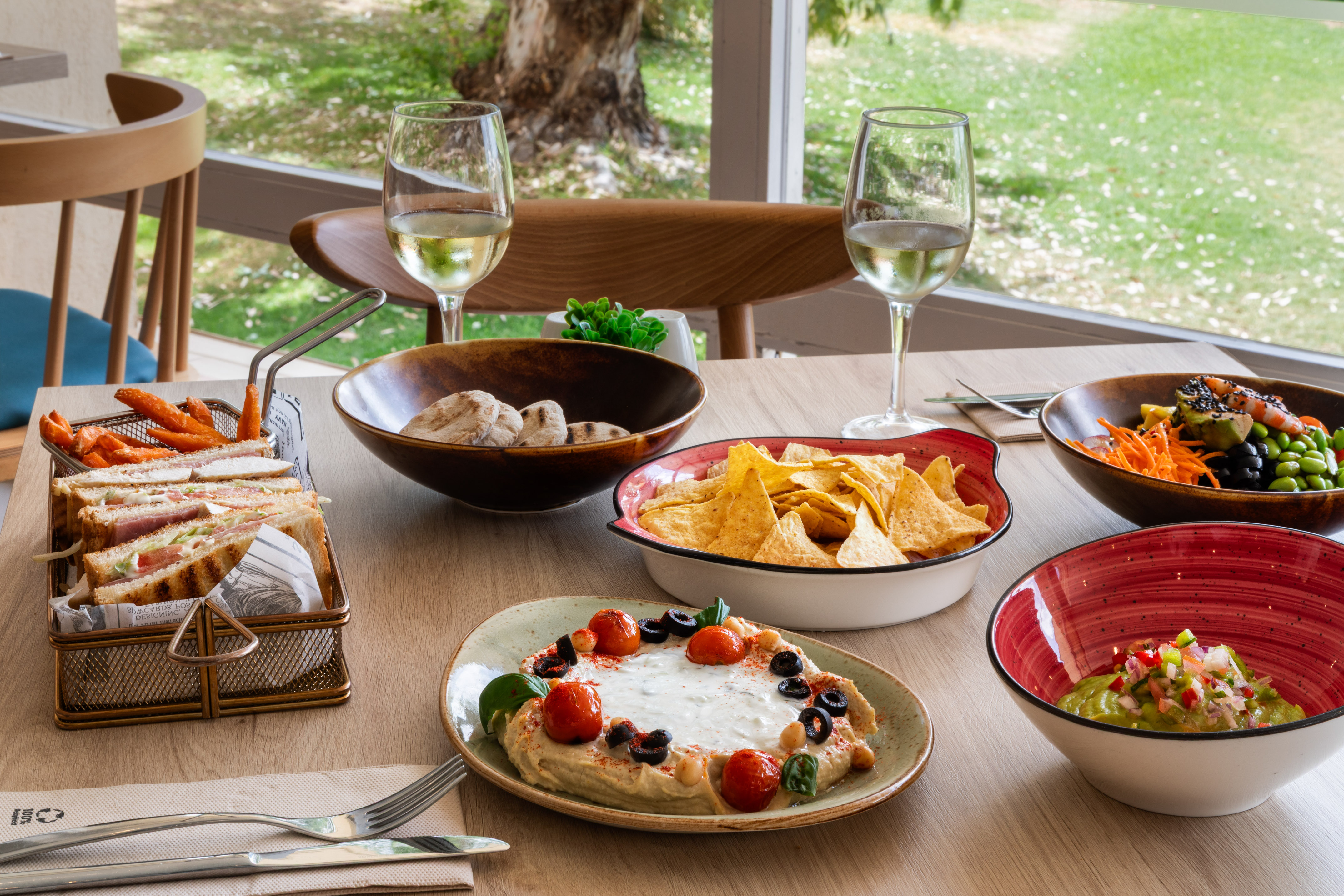 Restaurant lunch spread: hummus, guacamole, nachos, sandwiches, wine.
