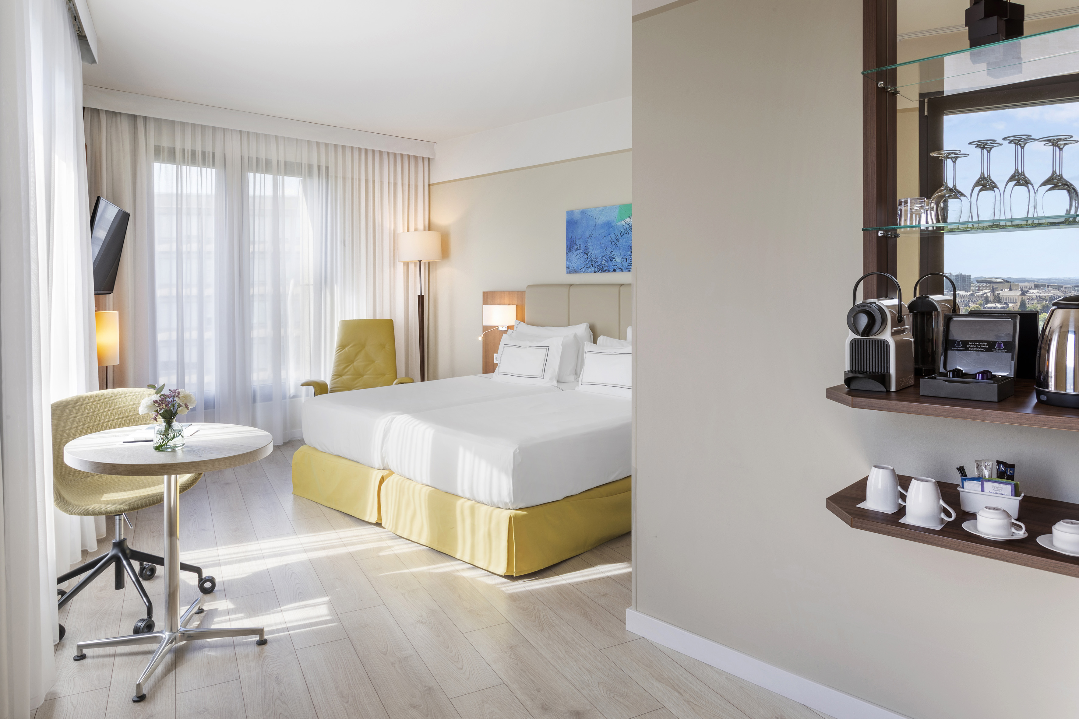 Bright hotel room with twin beds, coffee machine, and city view.