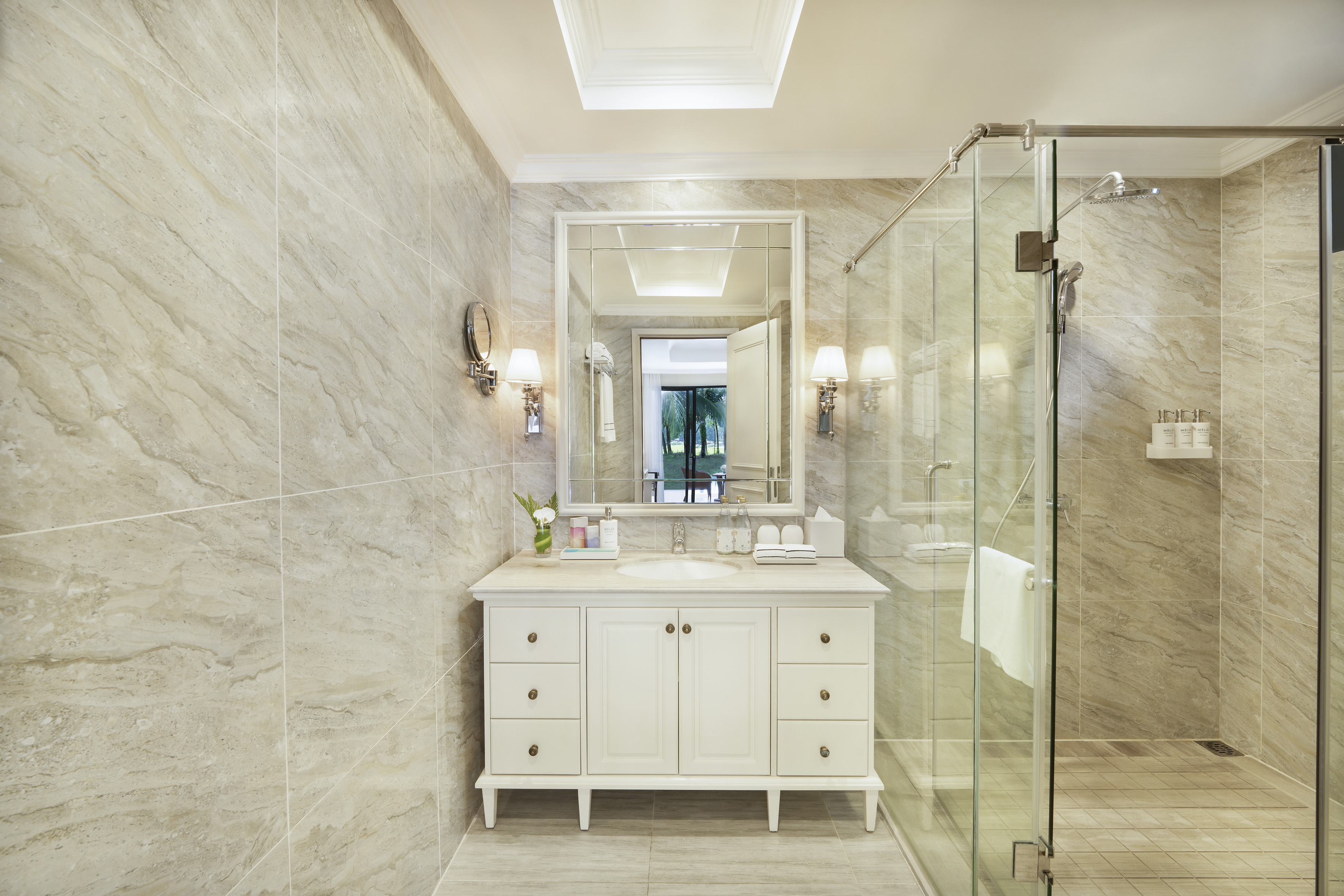 Luxury hotel bathroom: white vanity, marble tiles, large mirror, glass shower.