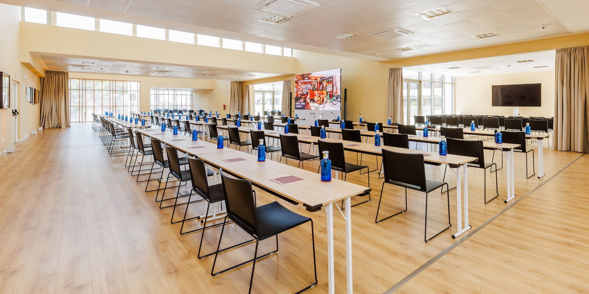 Spacious conference room setup with tables, chairs, water bottles, and large screen.