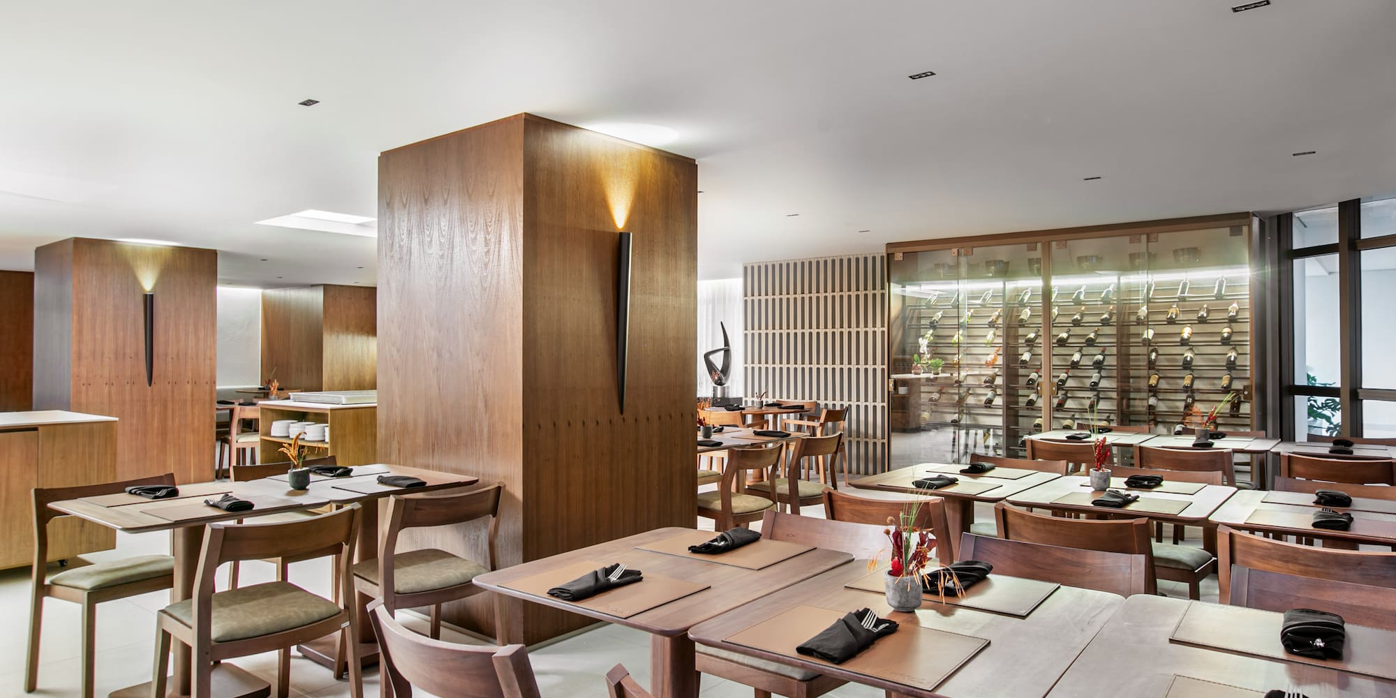 Modern restaurant dining room with wood furniture and illuminated wine wall.