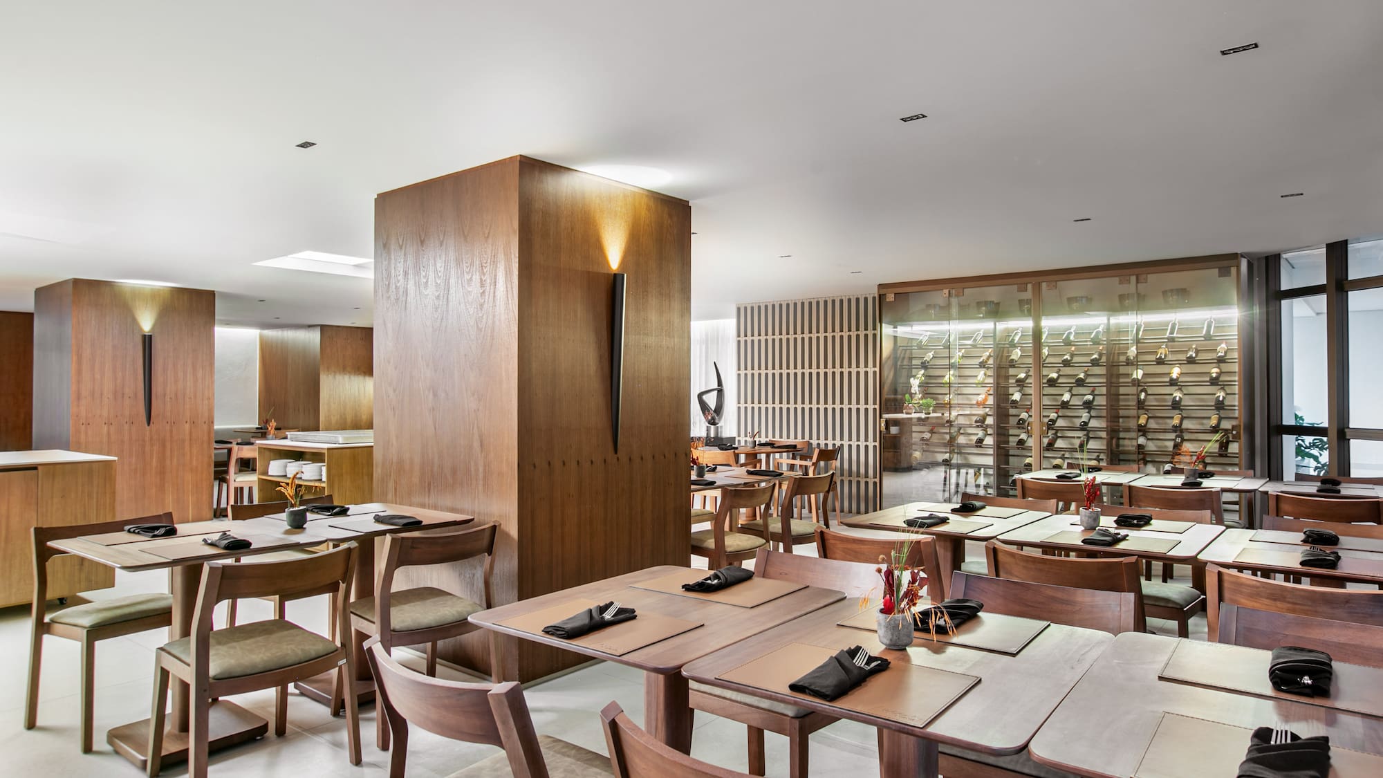 Modern restaurant dining room with wood furniture and illuminated wine wall.