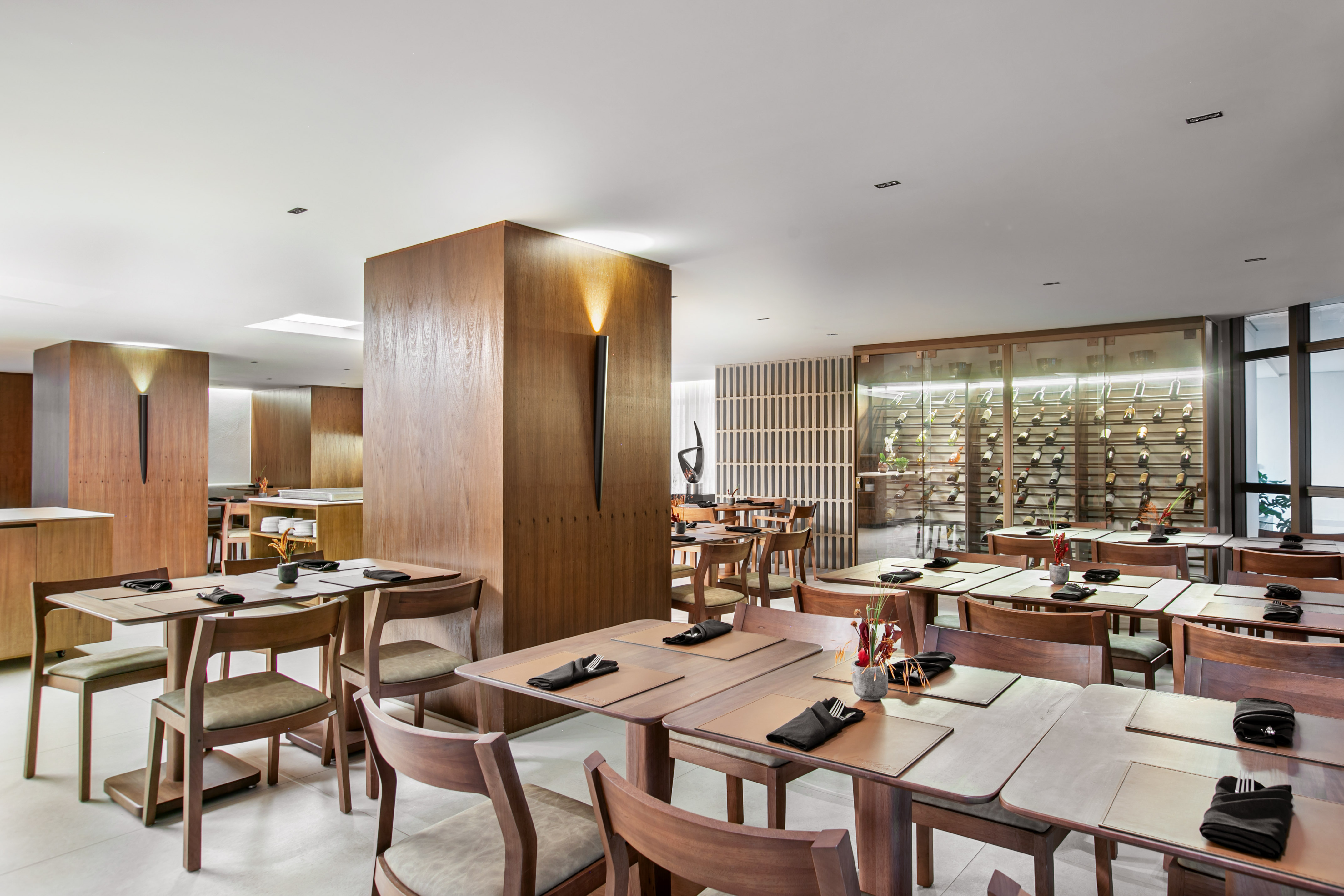 Modern restaurant dining room with wood furniture and illuminated wine wall.