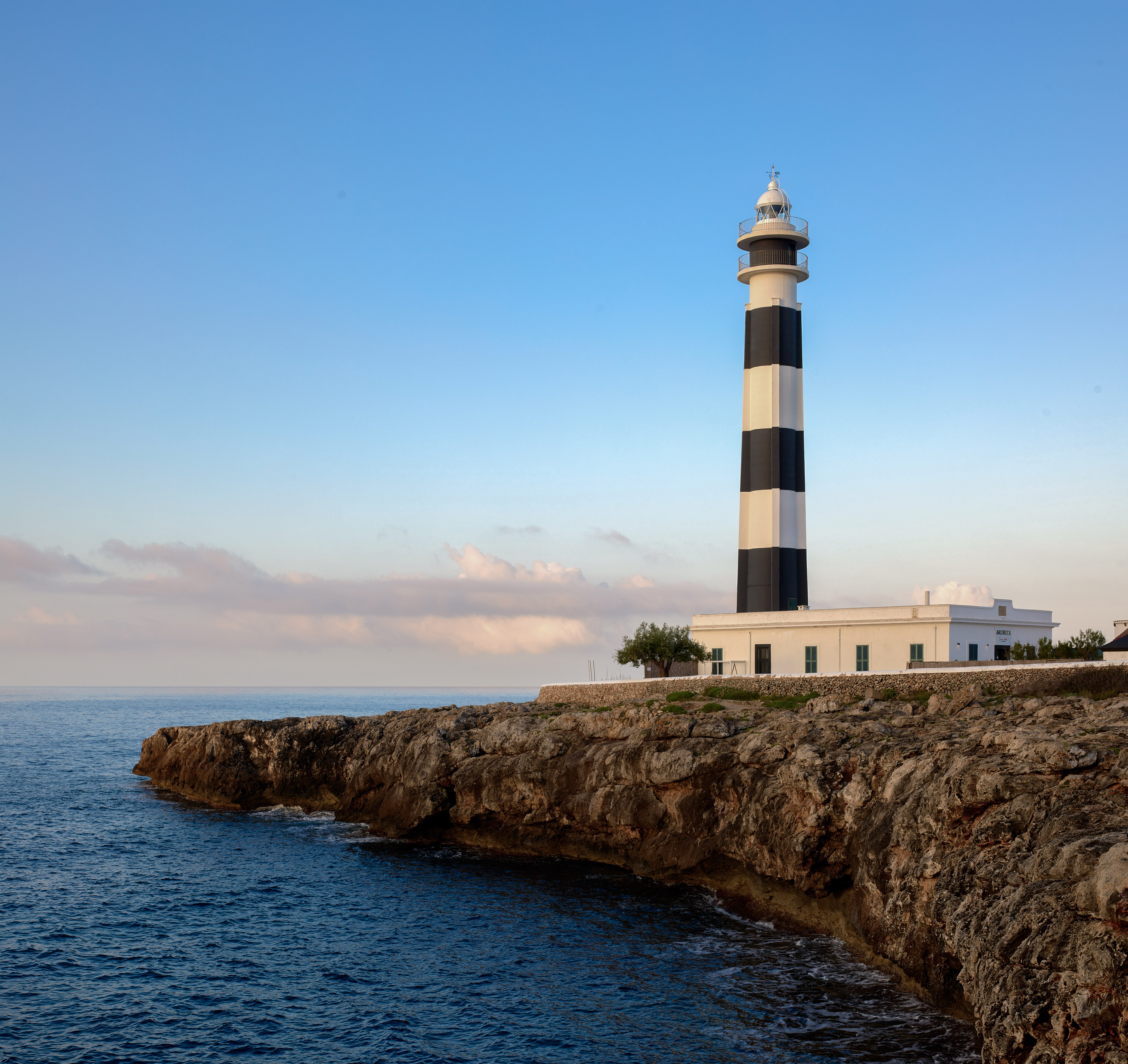 Black and white lighthouse on rugged coastal cliffs under a clear sky.