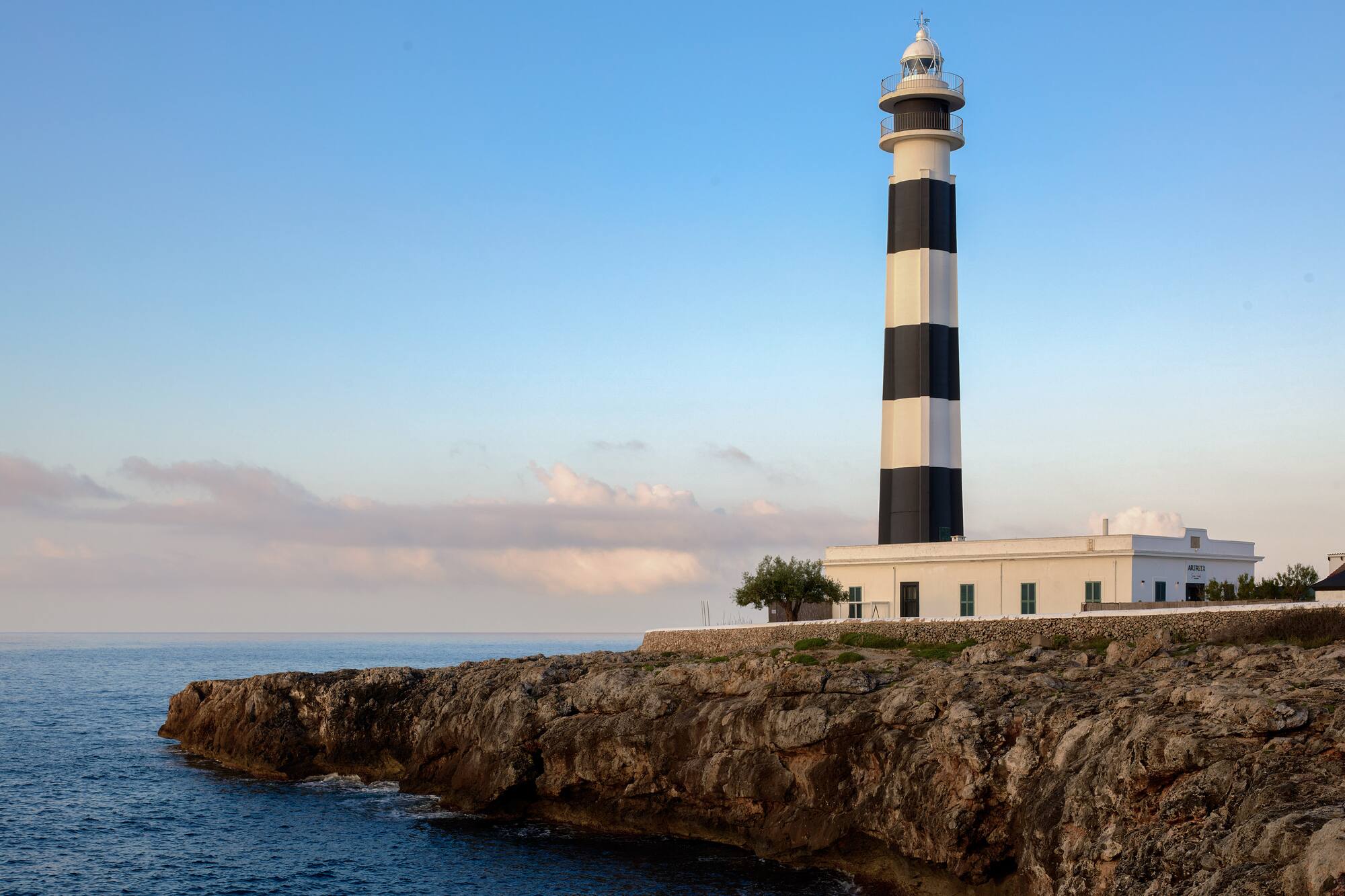 Black and white lighthouse on rugged coastal cliffs under a clear sky.