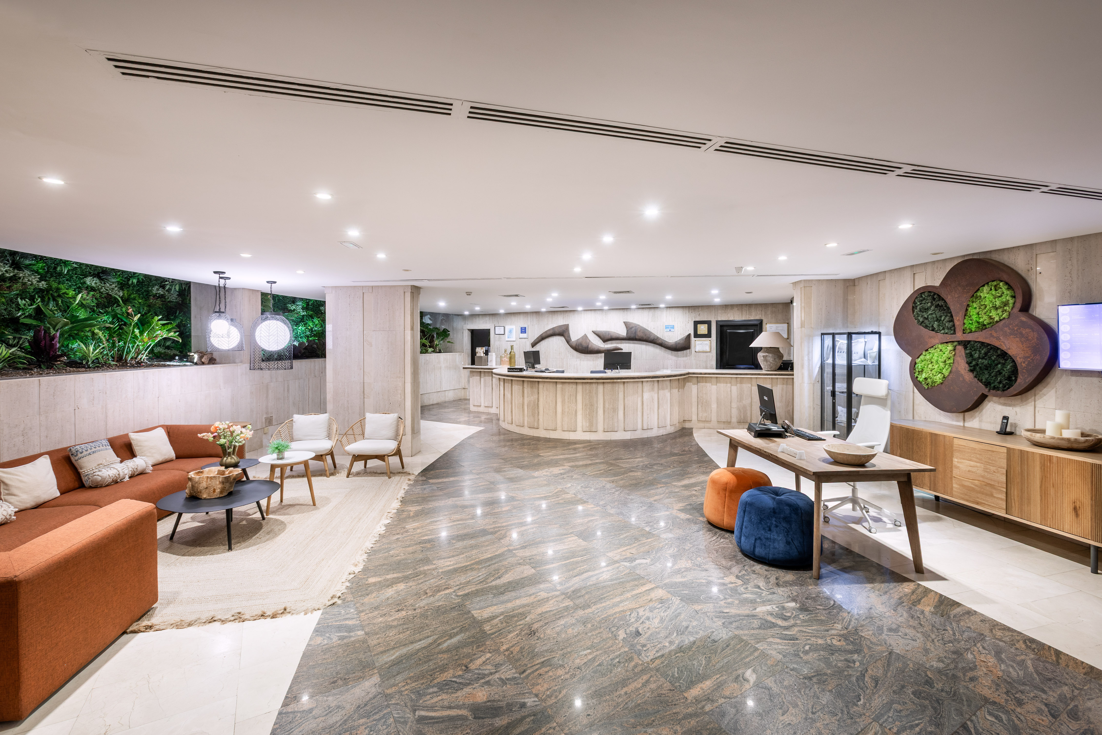 Modern hotel lobby with reception desk, cozy lounge seating, and lush indoor plants.