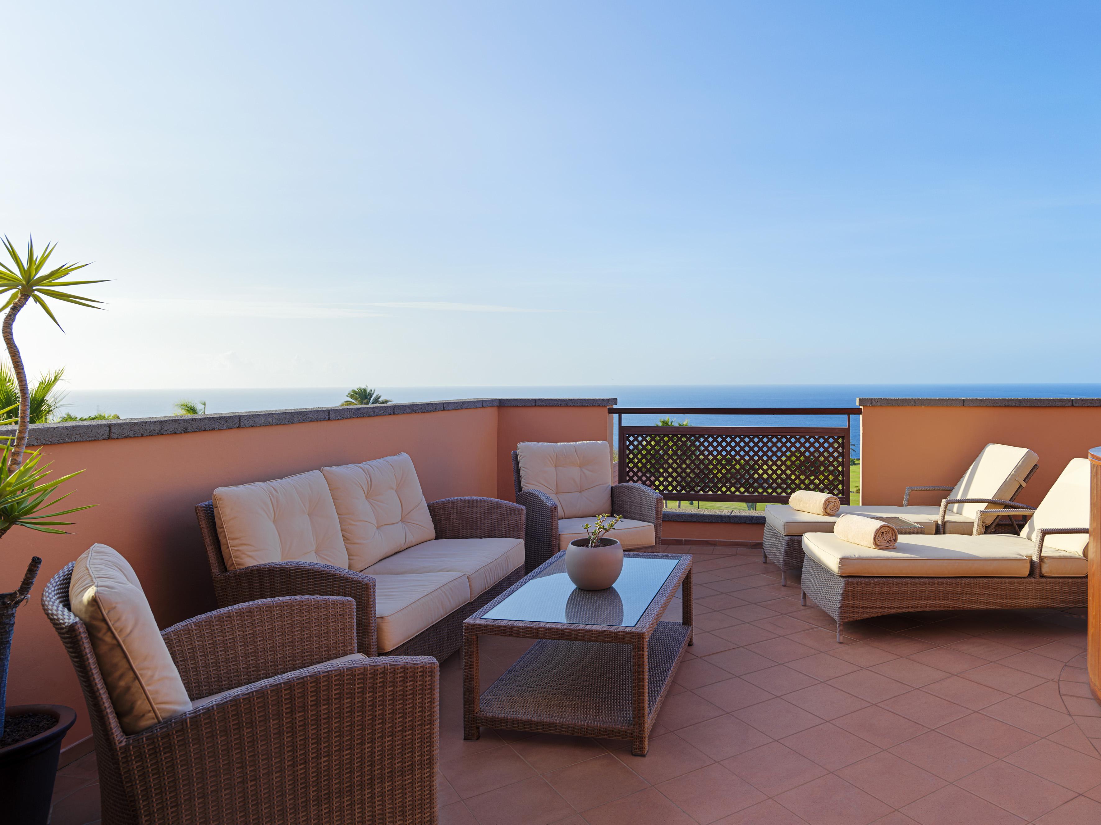 Outdoor terrace with ocean view, wicker patio furniture, and sunbeds.
