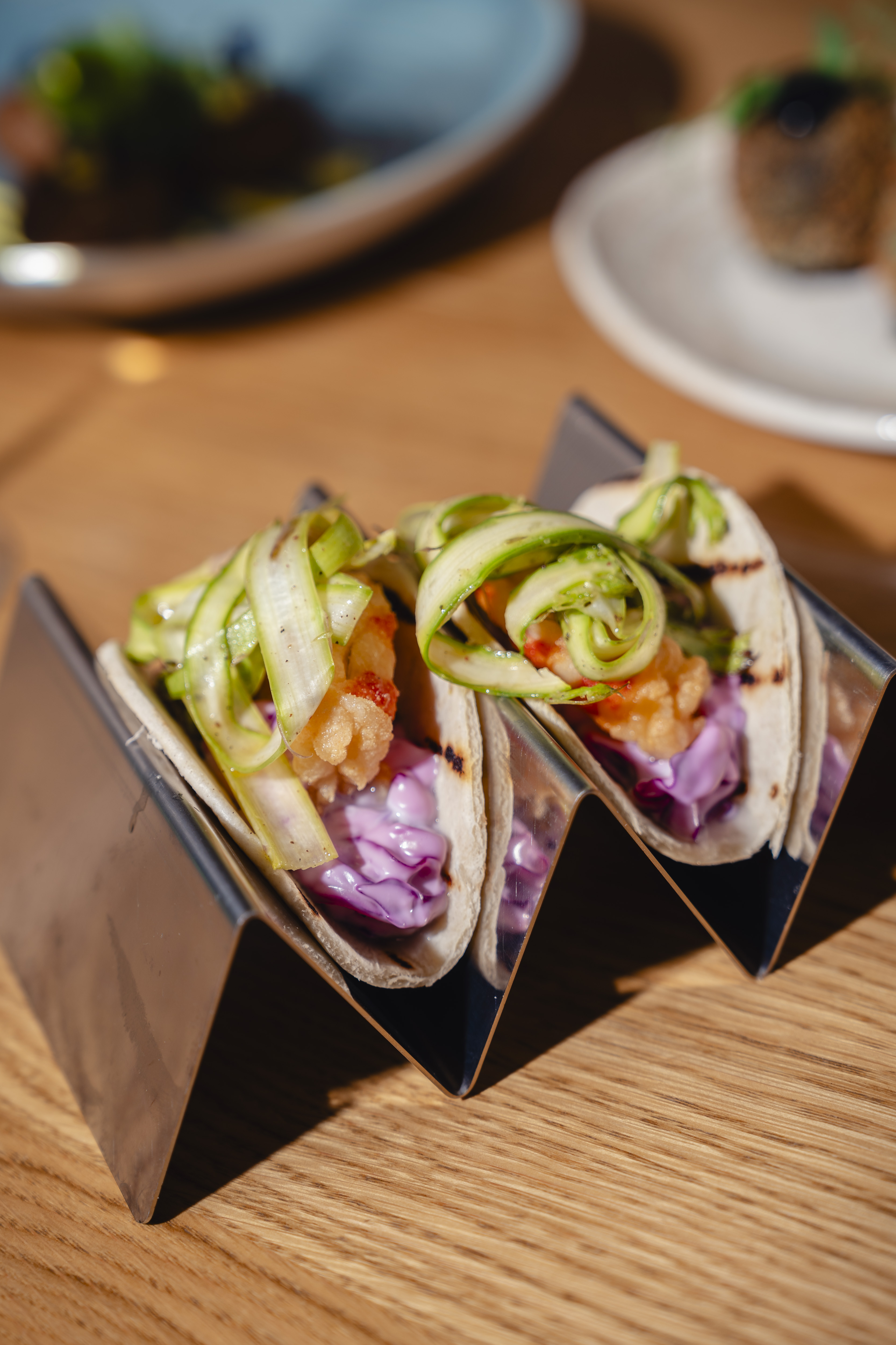 Shrimp tacos with purple slaw and zucchini ribbons in a metal holder.