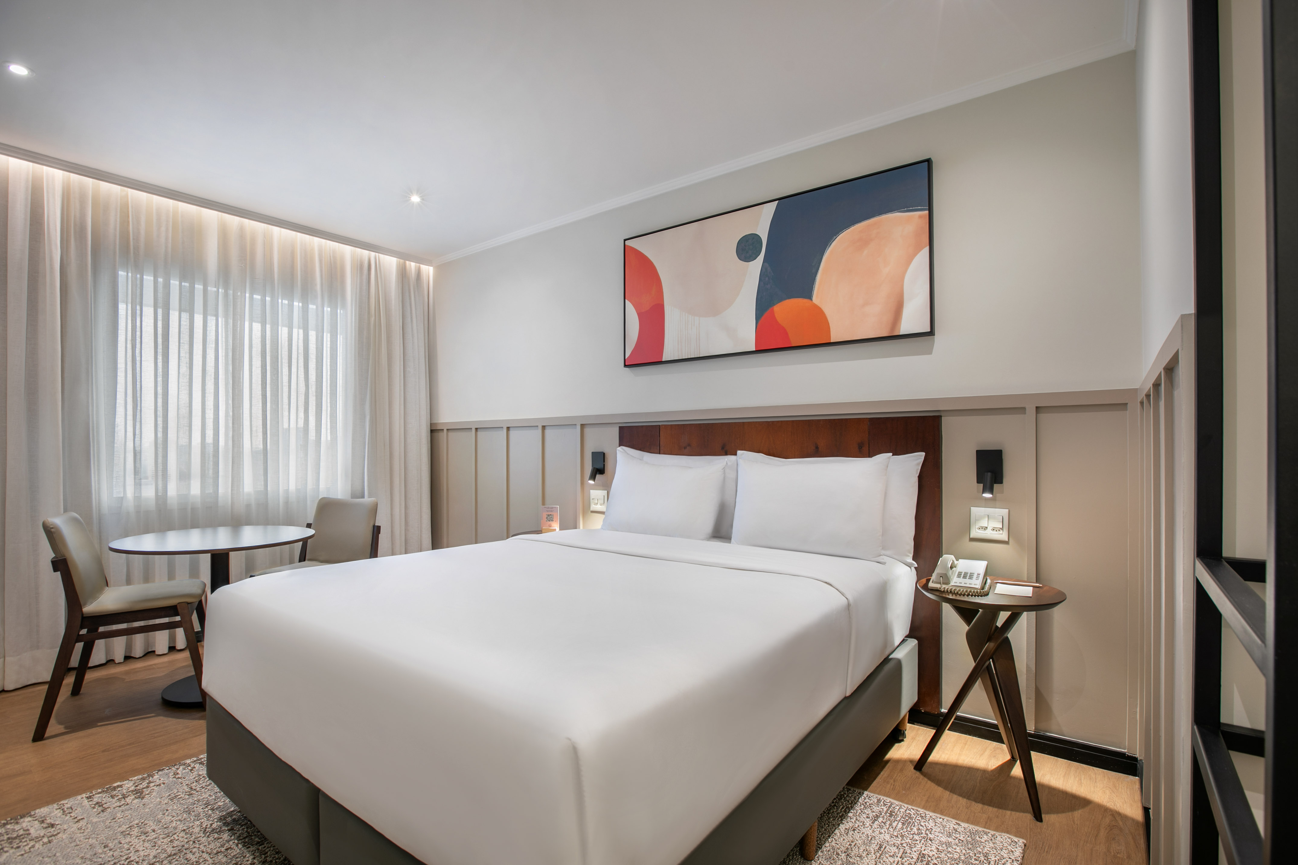Modern hotel room featuring a king bed, abstract art, and a small dining area.